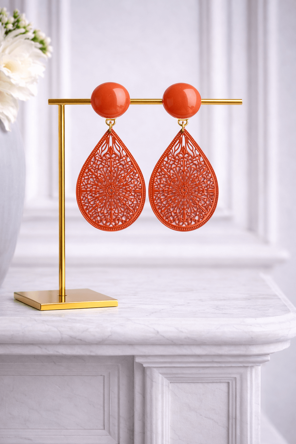 Orange Clip-Ohrringe mit rundem, glänzendem Stecker und tropfenförmigem Anhänger aus filigran gearbeitetem Metall, freigestellt vor weißem Hintergrund.