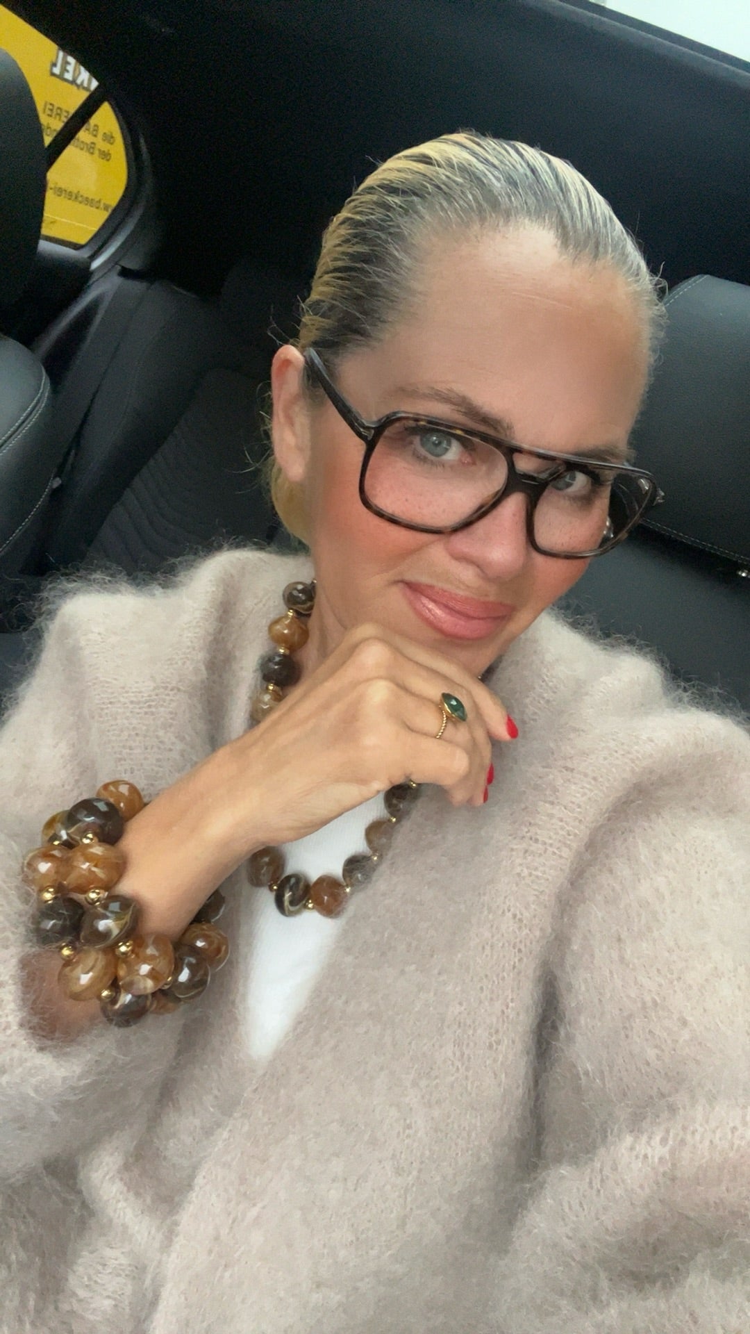 Frau sitzt im Auto, trägt zwei gr0ße braune Armbänder und braune Kette mit Ring.