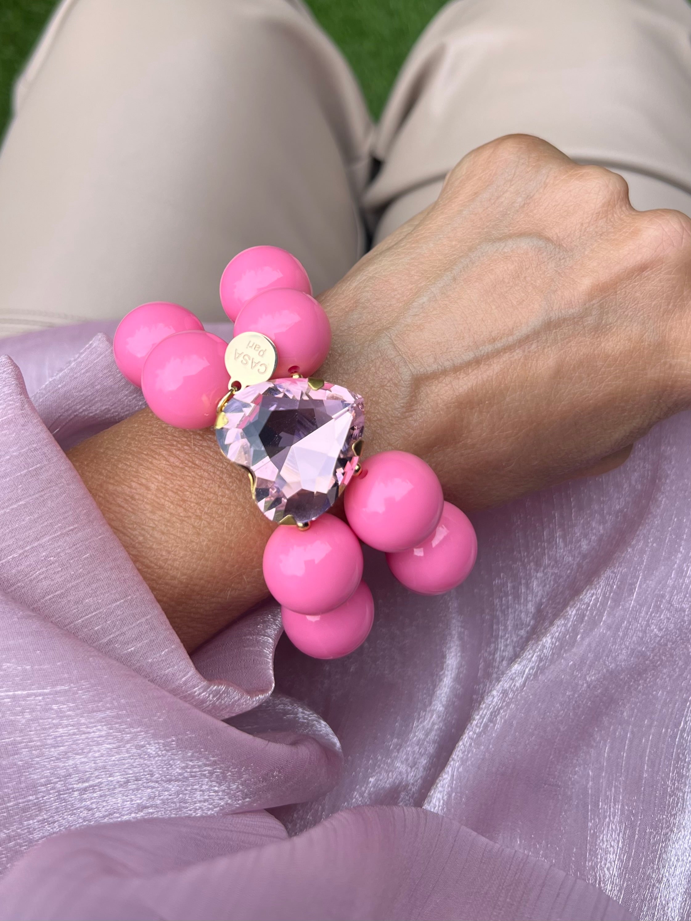 Handgelenk mit pinken Armband aus großen, glänzenden Perlen und einem herzförmigen, rosa Kristall in der Mitte.