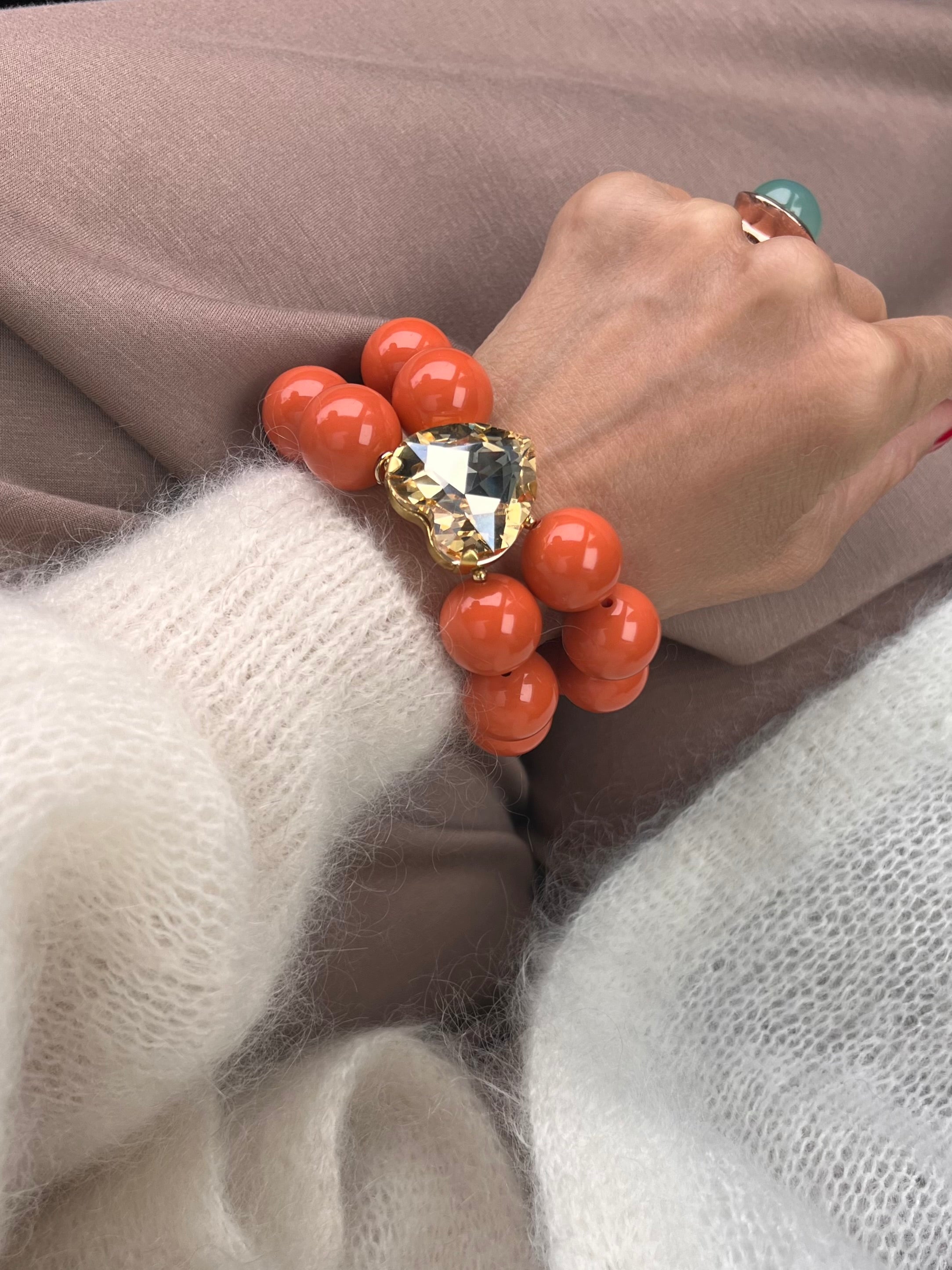 Armband in Mandarine Farben mit großem Herzschmuckstein, und großem Ring. Am Handgelenk auf beigem Stoff fotografiert.