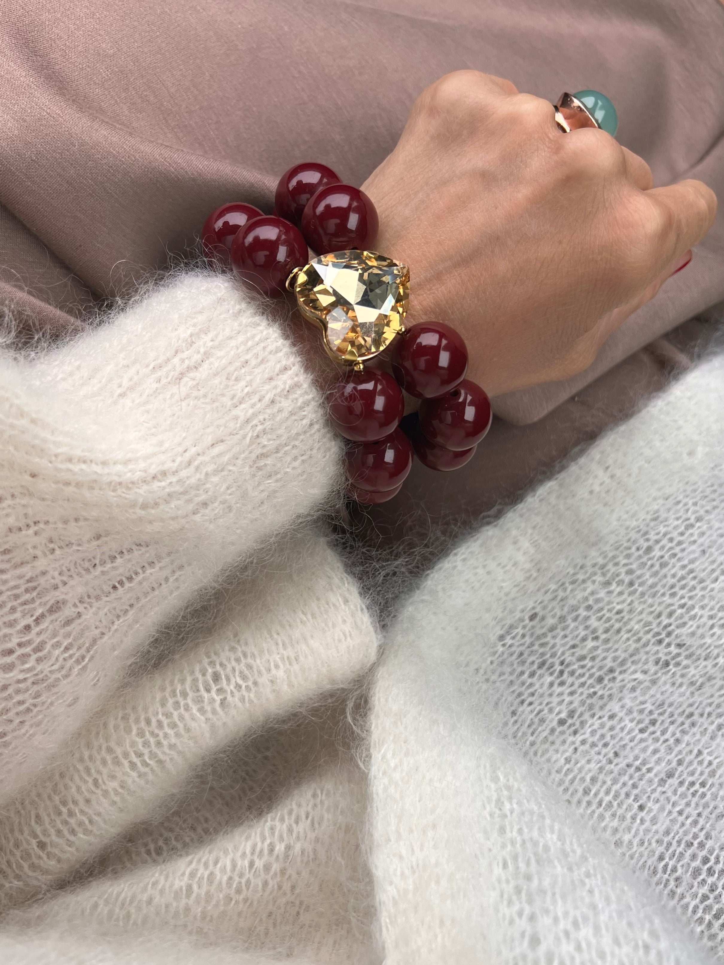 Armband in Burgund braun mit großem Herzschmuckstein, und großem Ring. Am Handgelenk auf beigem Stoff fotografiert.