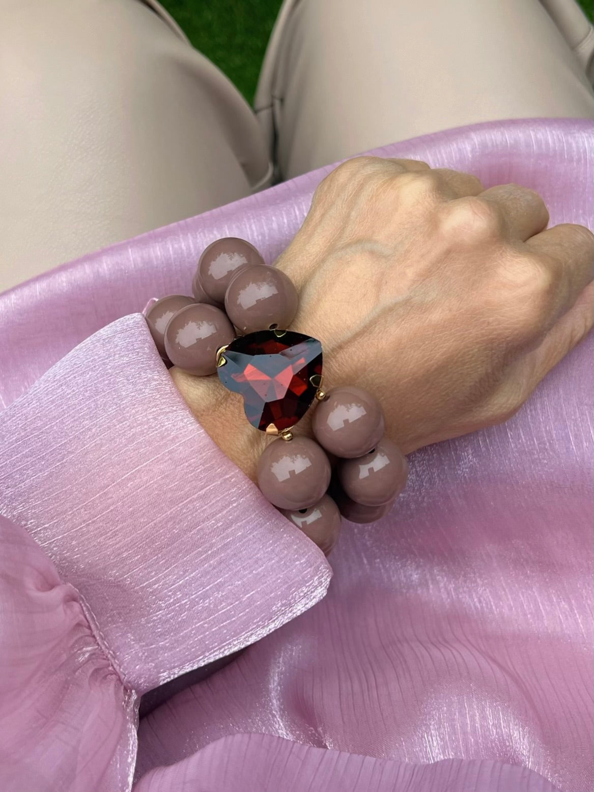 Armband in Taupe mit großem Herzschmuckstein. Am Handgelenk auf rosa Stoff fotografiert.