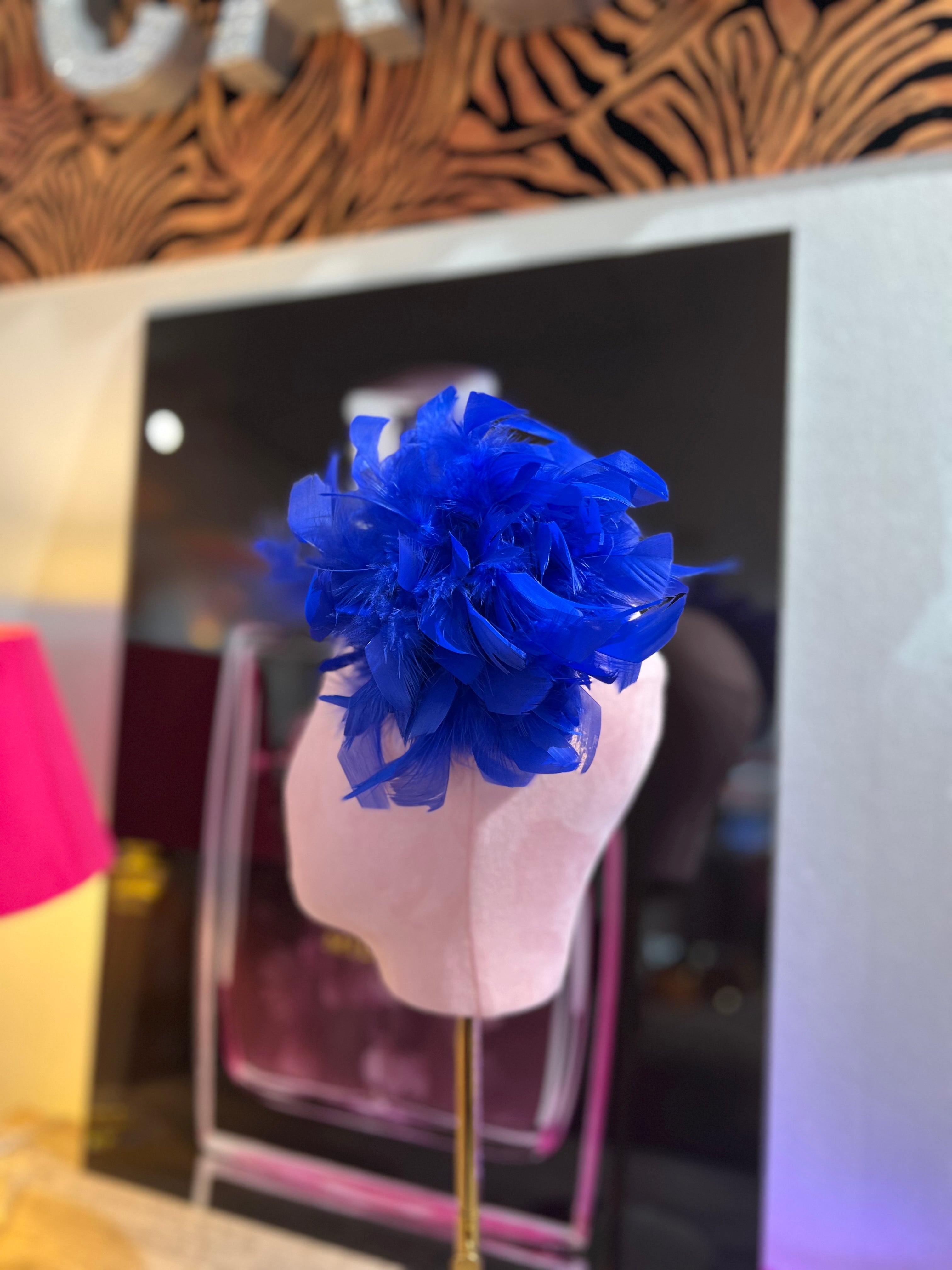 Leuchtende blaue Federbrosche, kunstvoll drapiert, präsentiert auf einem rosa Samt Kopf vor einer stilvollen Kulisse.
