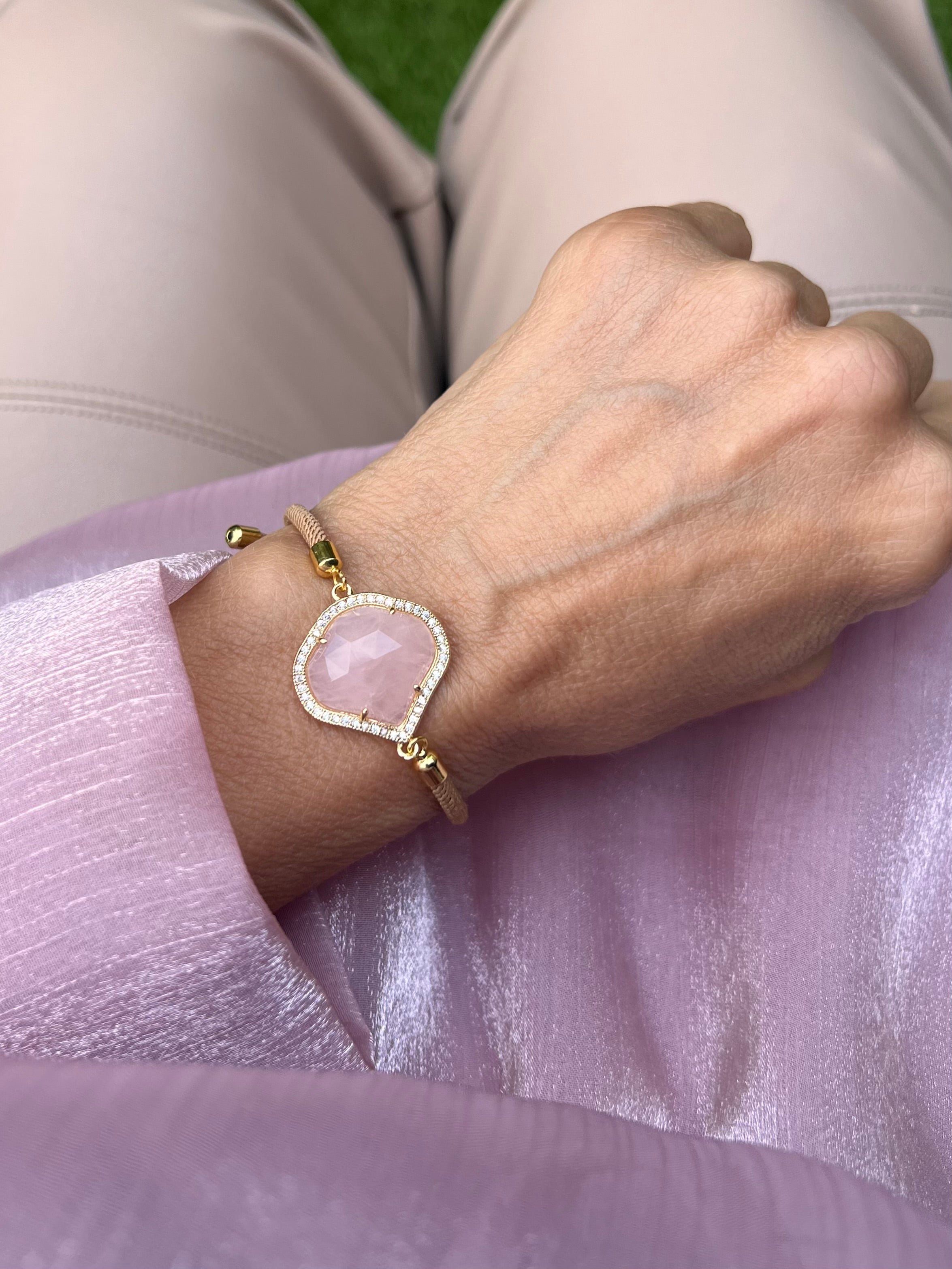 Beiges Armband mit rosa Schmuckstein an Hand getragen. Auf rosa Stoff fotografiert.