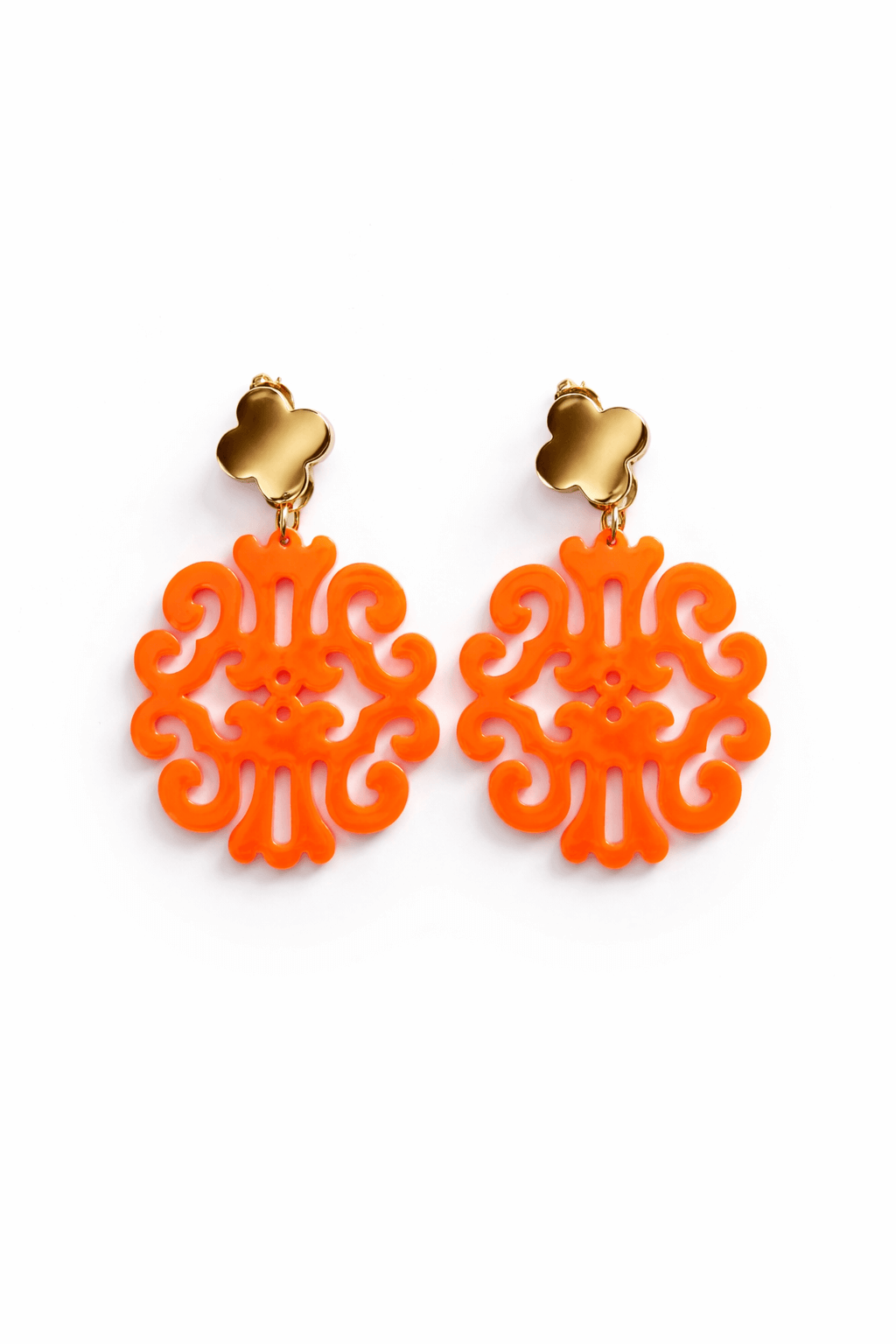 Paar hängende Ohrringe mit goldfarbenem Kleeblatt-Stecker und orangem ornamental durchbrochenem Anhänger vor weißem Hintergrund.