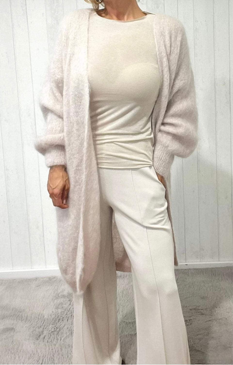 Frau trägt langen beigen Strickmantel mit beiger Hose und Shirt. Lässig fotografiert.