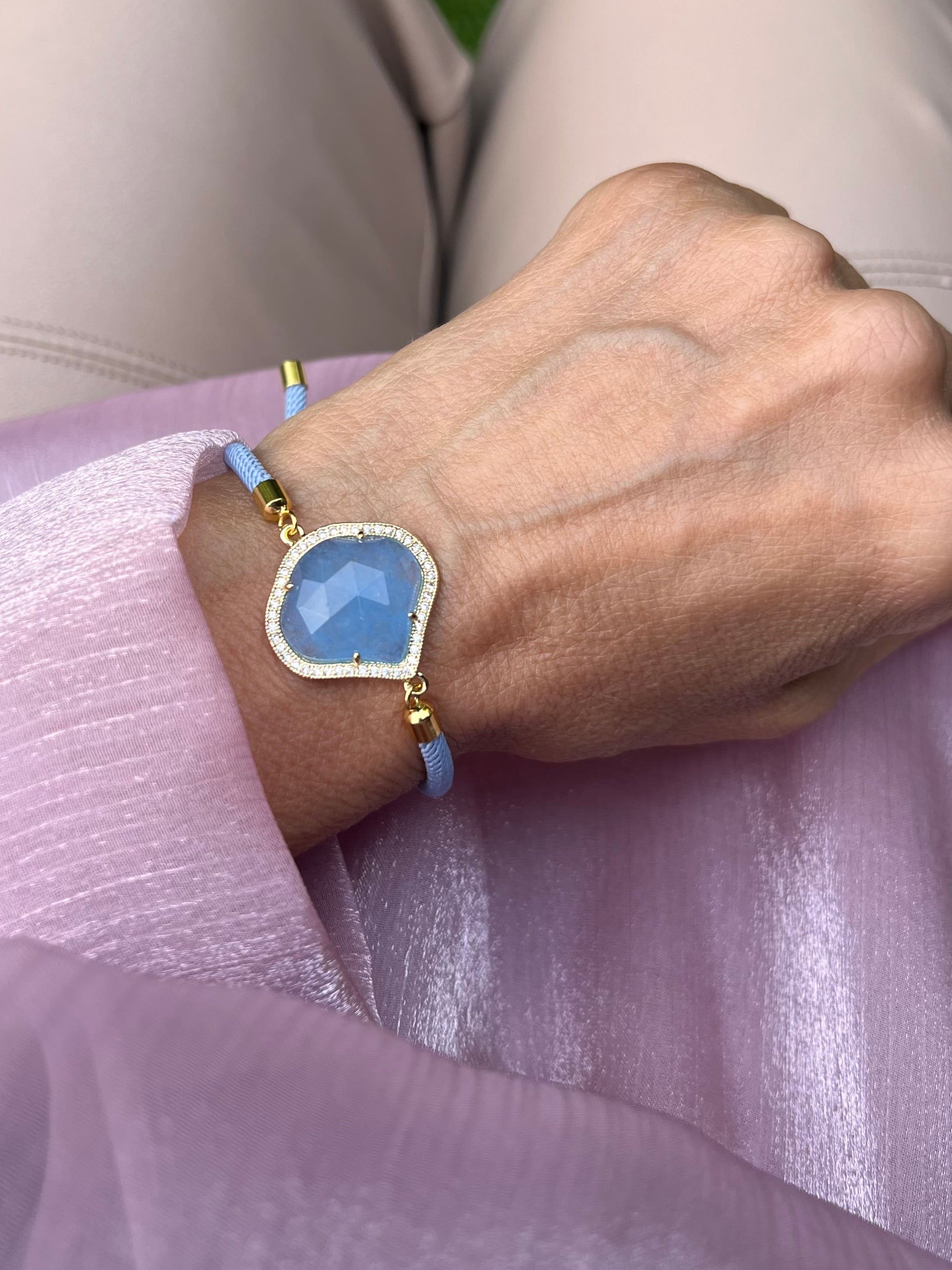 Blaues Armband mit blauem Schmuckstein an Hand getragen. Auf rosa Stoff fotografiert.