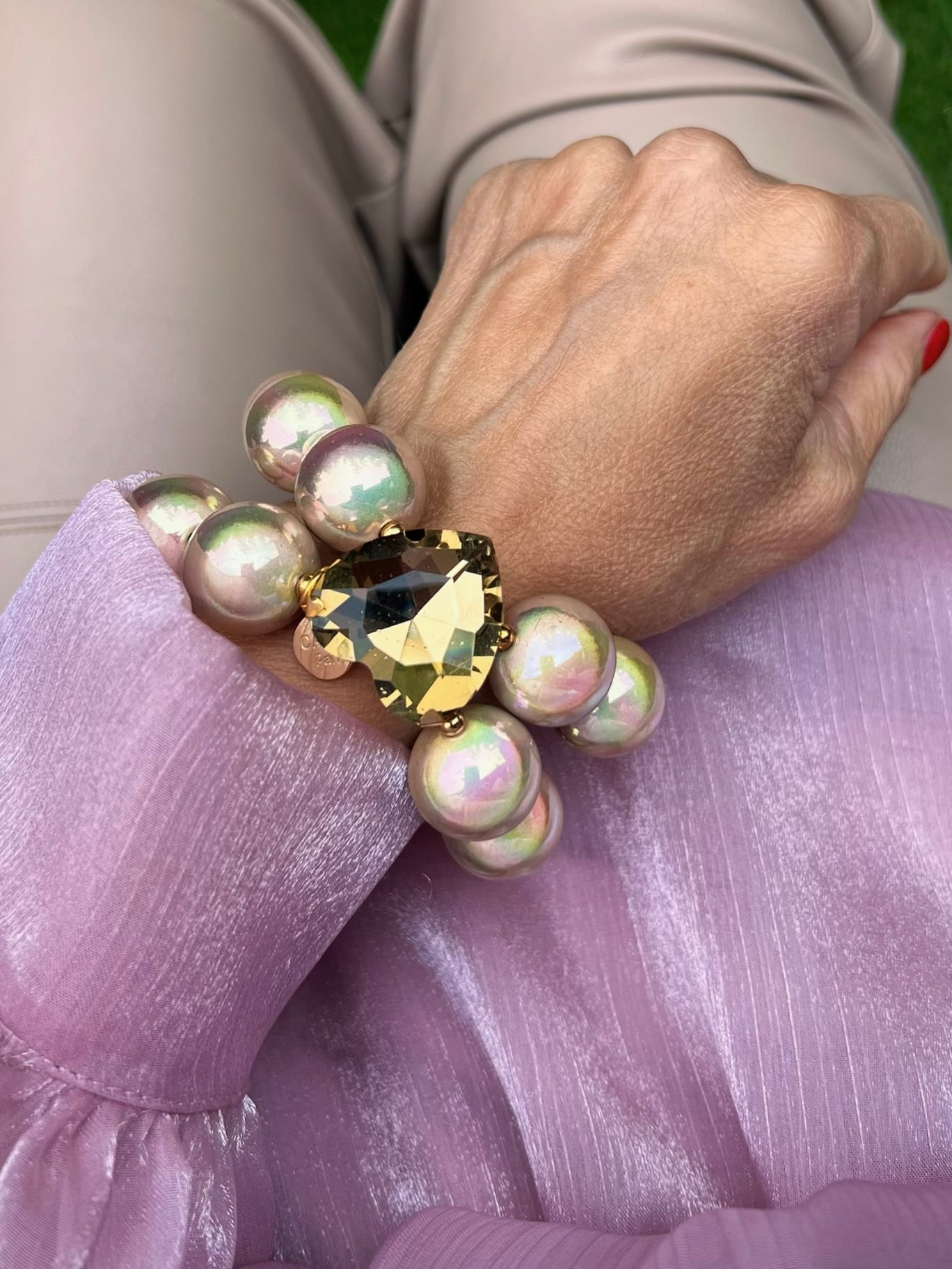 Armband in Opalfarben mit großem Herzschmuckstein. Am Handgelenk auf rosa Stoff fotografiert.