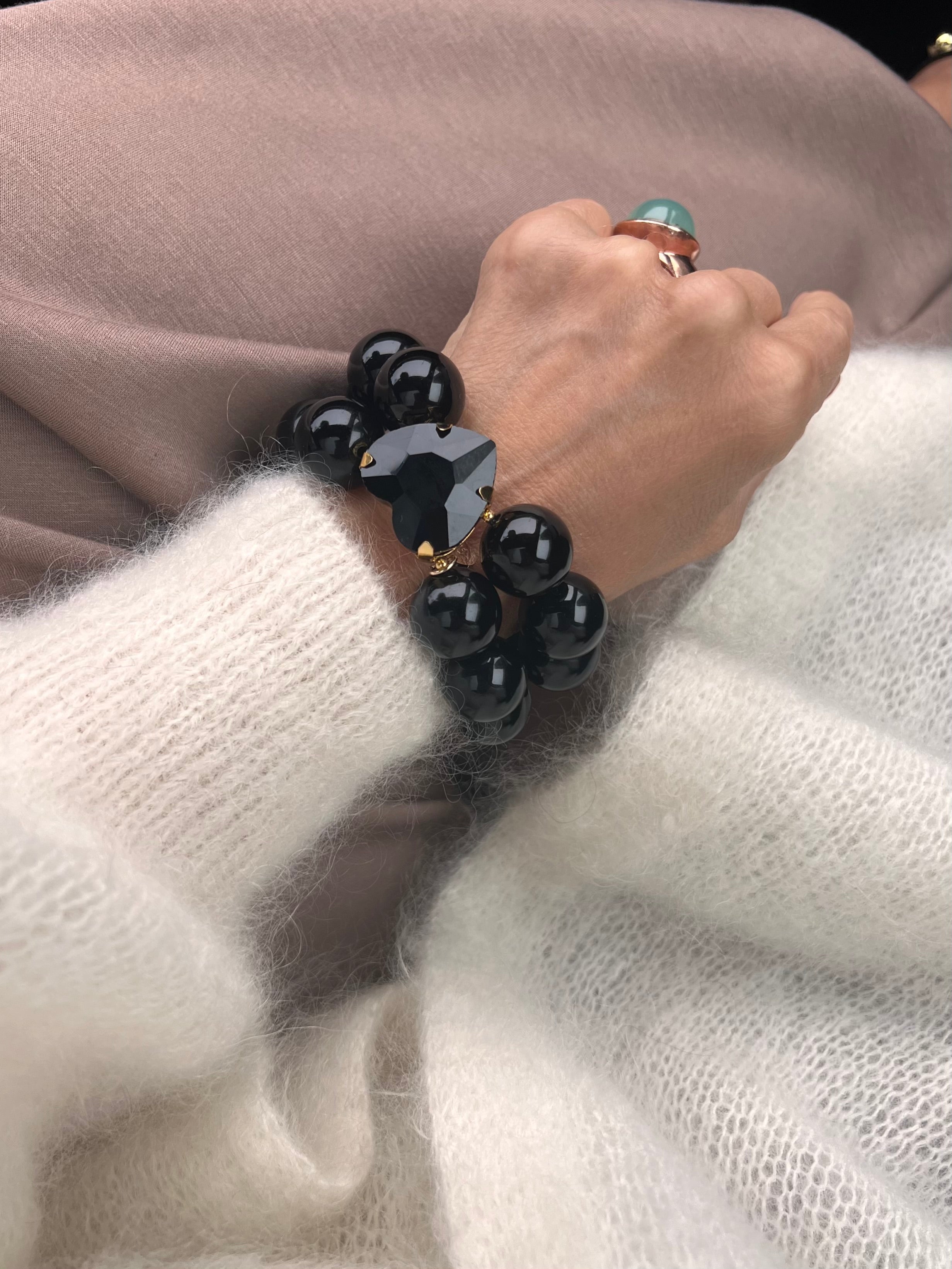 Armband in Schwarz mit großem Herzschmuckstein, und großem Ring. Am Handgelenk auf beigem Stoff fotografiert.