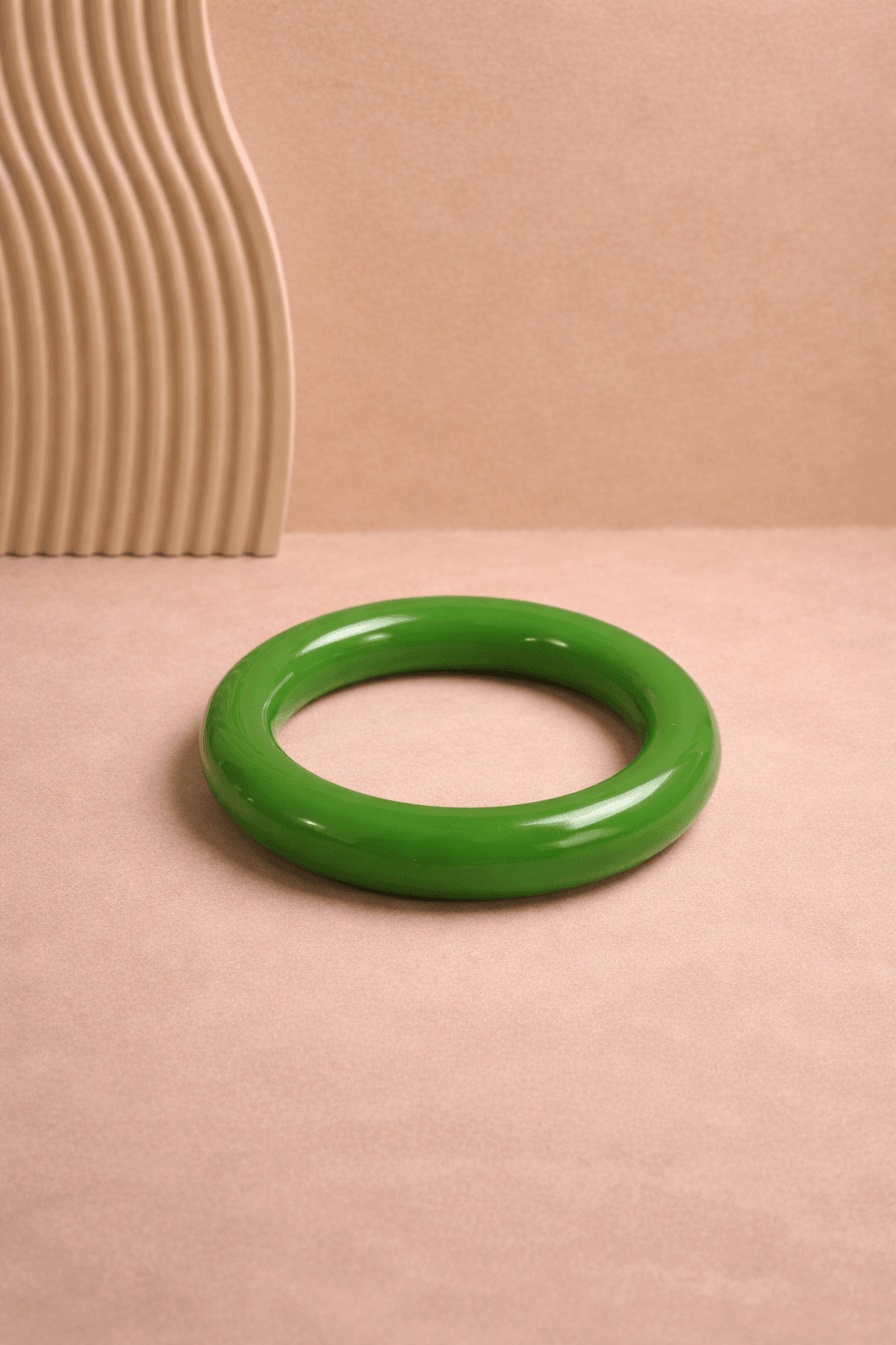 Heller grüner, glänzender Resin-Armreif liegt mittig auf weißem Untergrund; runde Form mit glatter Oberfläche, gleichmäßig ausgeleuchtet.