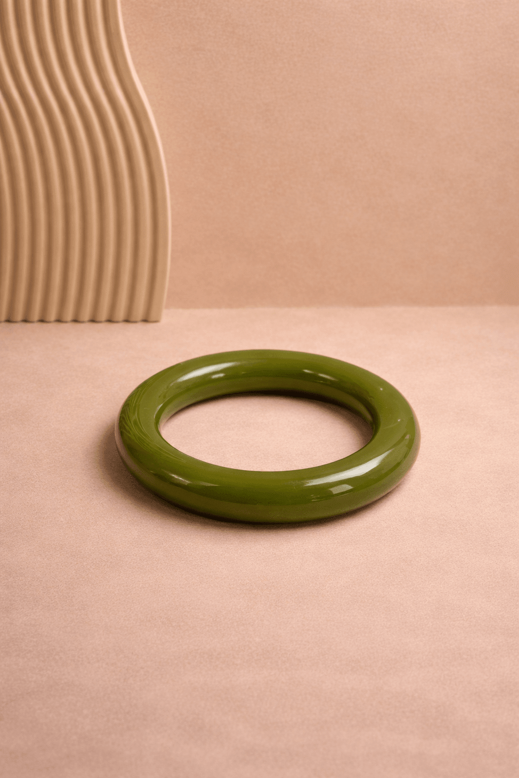 Oliv grüner, glänzender Resin-Armreif liegt mittig auf weißem Untergrund; runde Form mit glatter Oberfläche, gleichmäßig ausgeleuchtet.