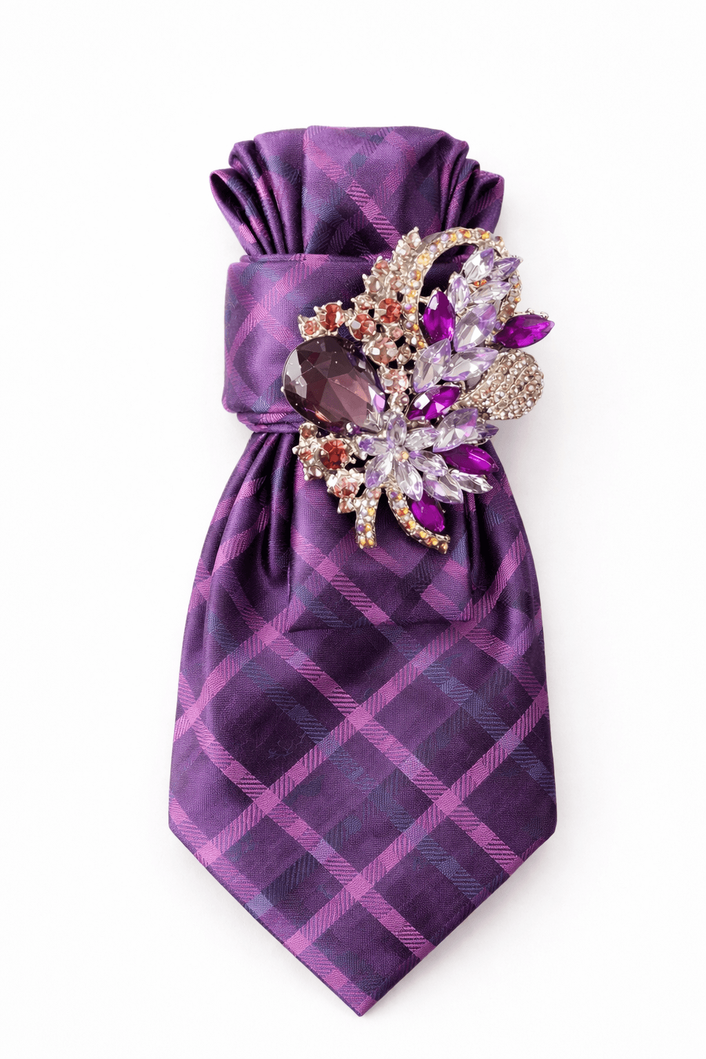 Lila Krawatte mit kariertem Muster in verschiedenen Violetttönen, dekorativ gebunden und mit einer großen, mehrfarbigen Brosche mit violetten und roséfarbenen Steinen verziert, freigestellt vor hellem Hintergrund.