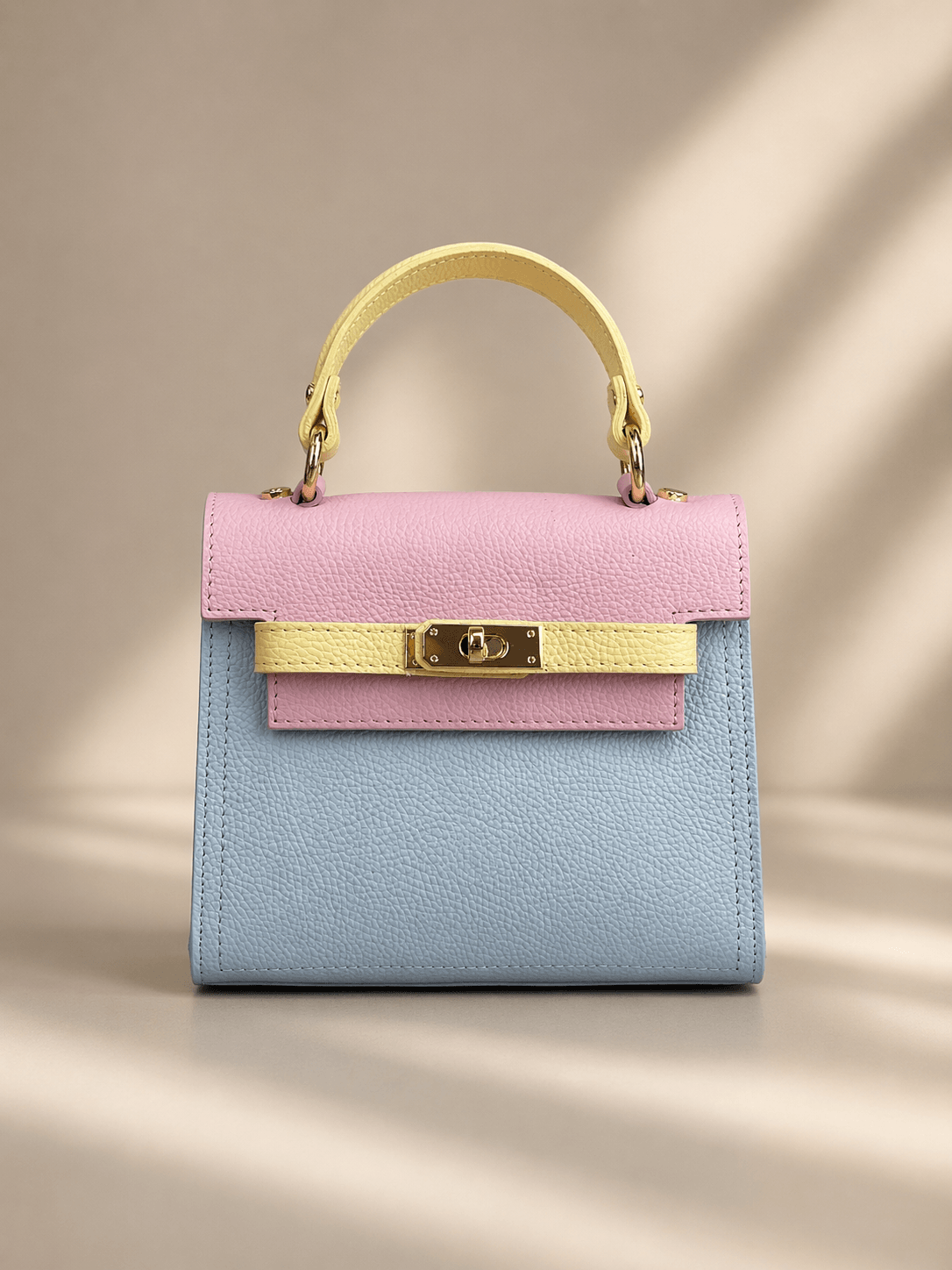 Kleine Ledertasche in Pastellfarben (Rosa, Gelb, Hellblau) mit Henkel und goldfarbenem Drehverschluss, freigestellt auf hellem Hintergrund.