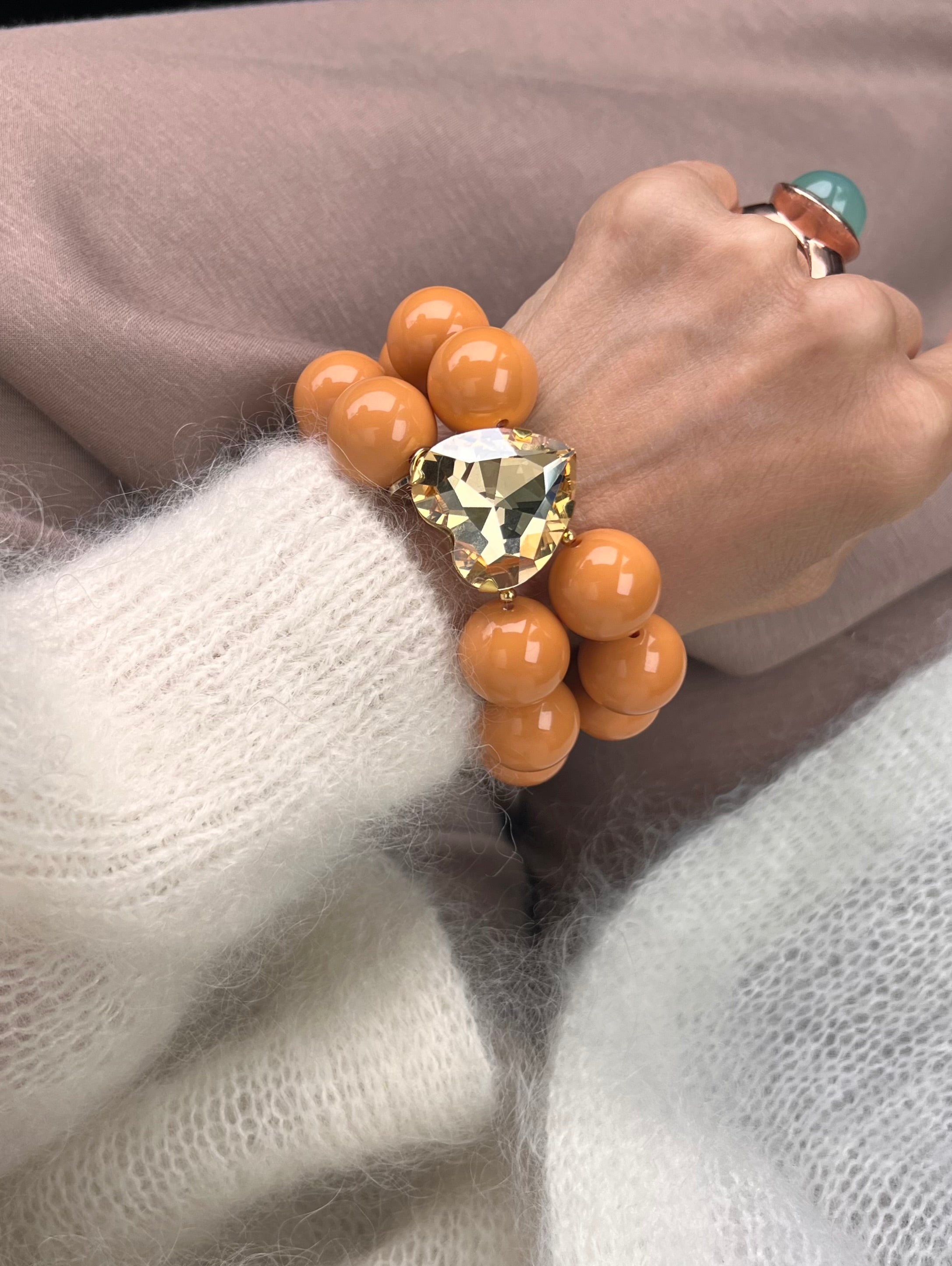 Armband in Senf Ocker Farben mit großem Herzschmuckstein, und großem Ring. Am Handgelenk auf beigem Stoff fotografiert.