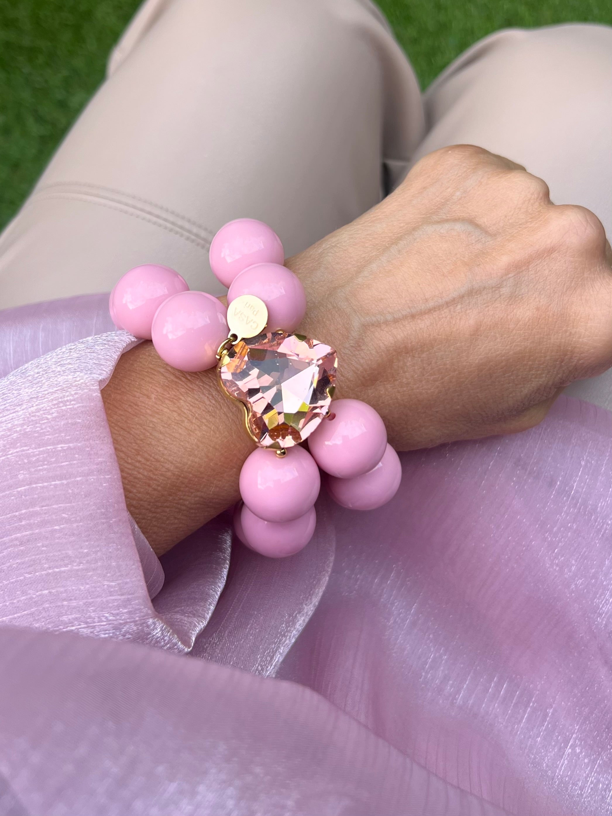Armband in Rosa mit rosa Kristallherz. An einem Handgelenk auf rosa Stoff fotografiert.