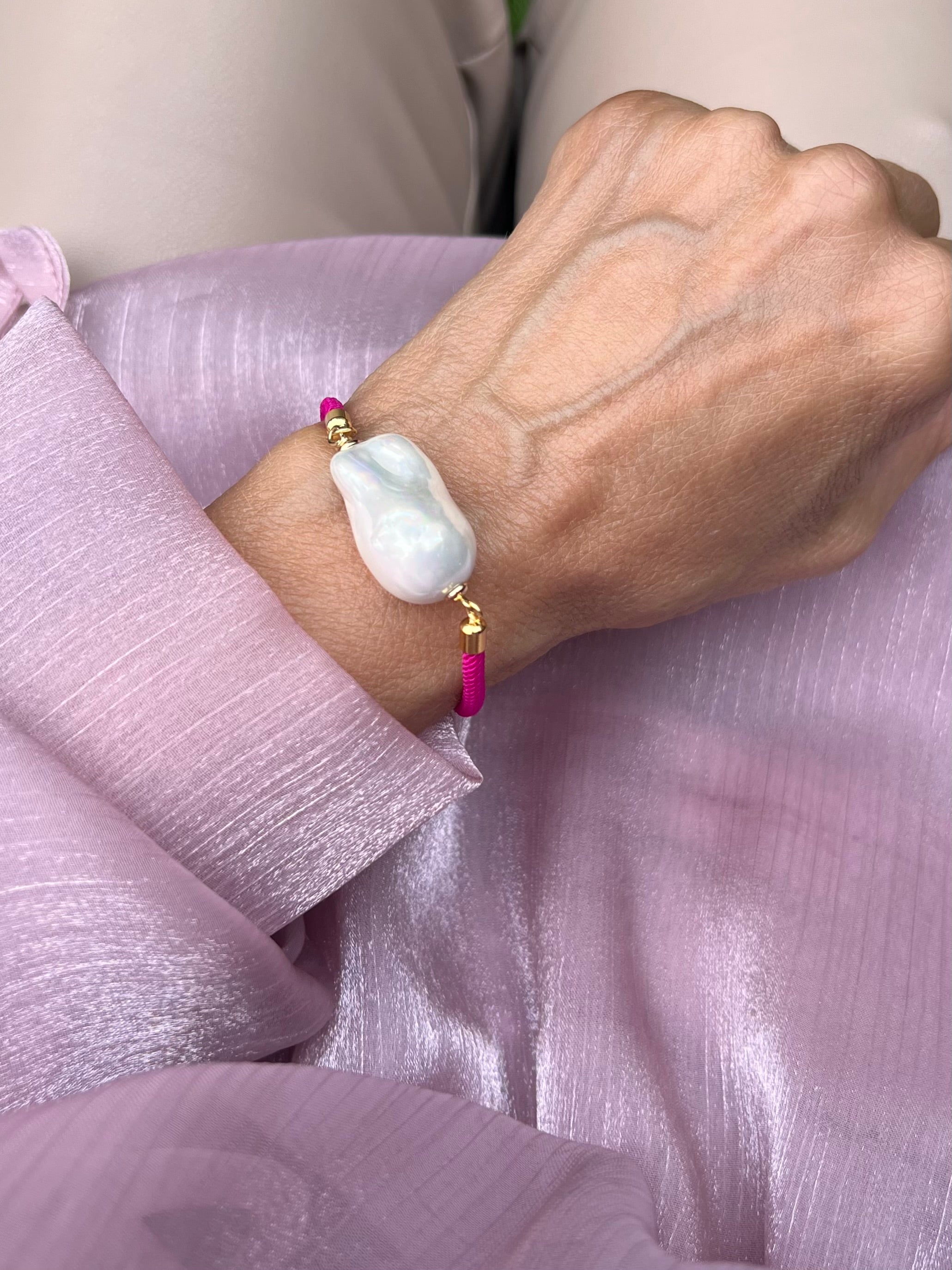 Handgelenk mit feinem pinken
 Armband und einer Barockperle mit goldenen Details. Auf rosa Stoff fotografiert.