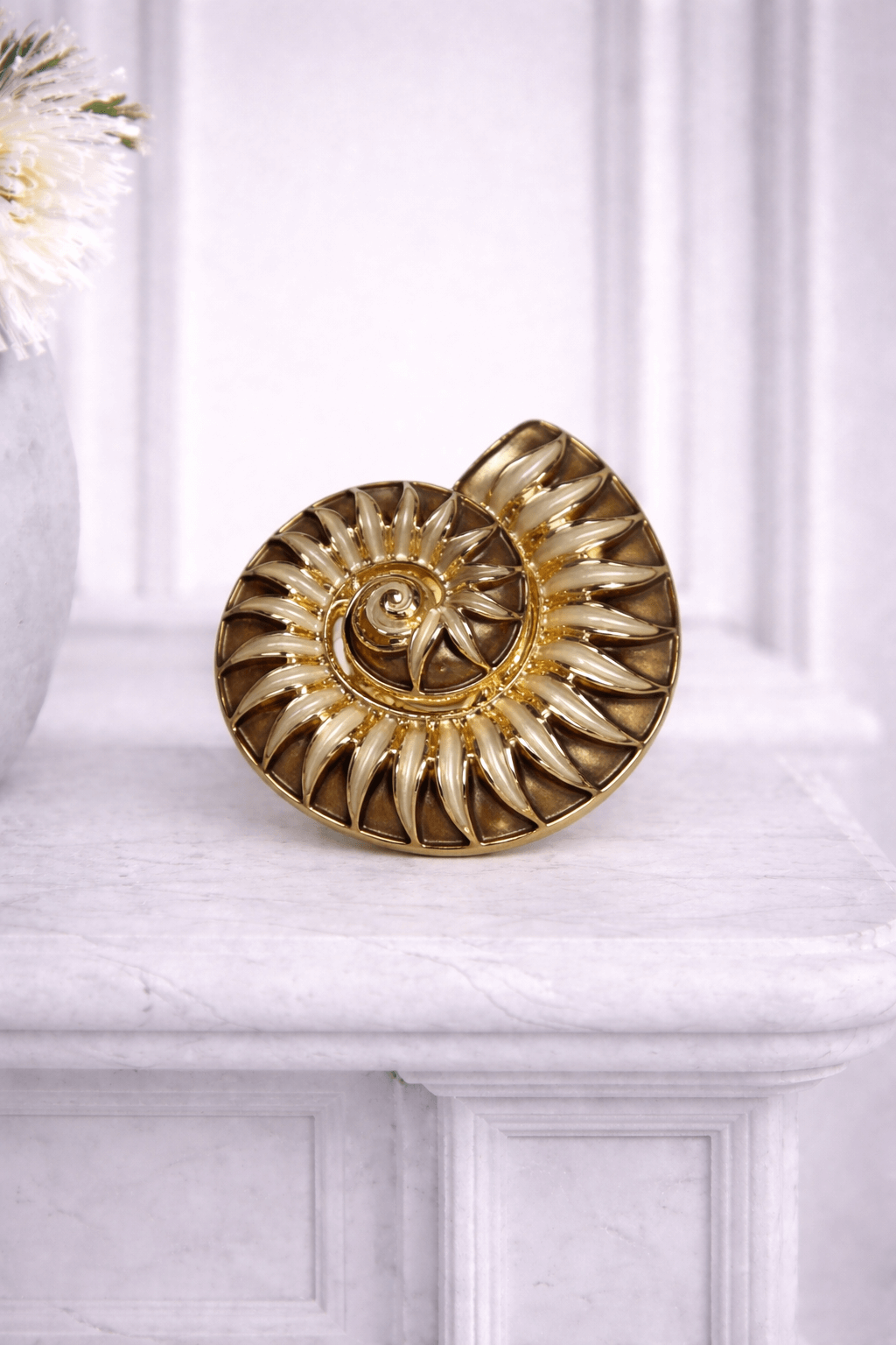 Goldfarbene Magnetbrosche in Spiralform mit emaillierten Details in Braun und Beige Tönen, fotografiert vor hellem Hintergrund.