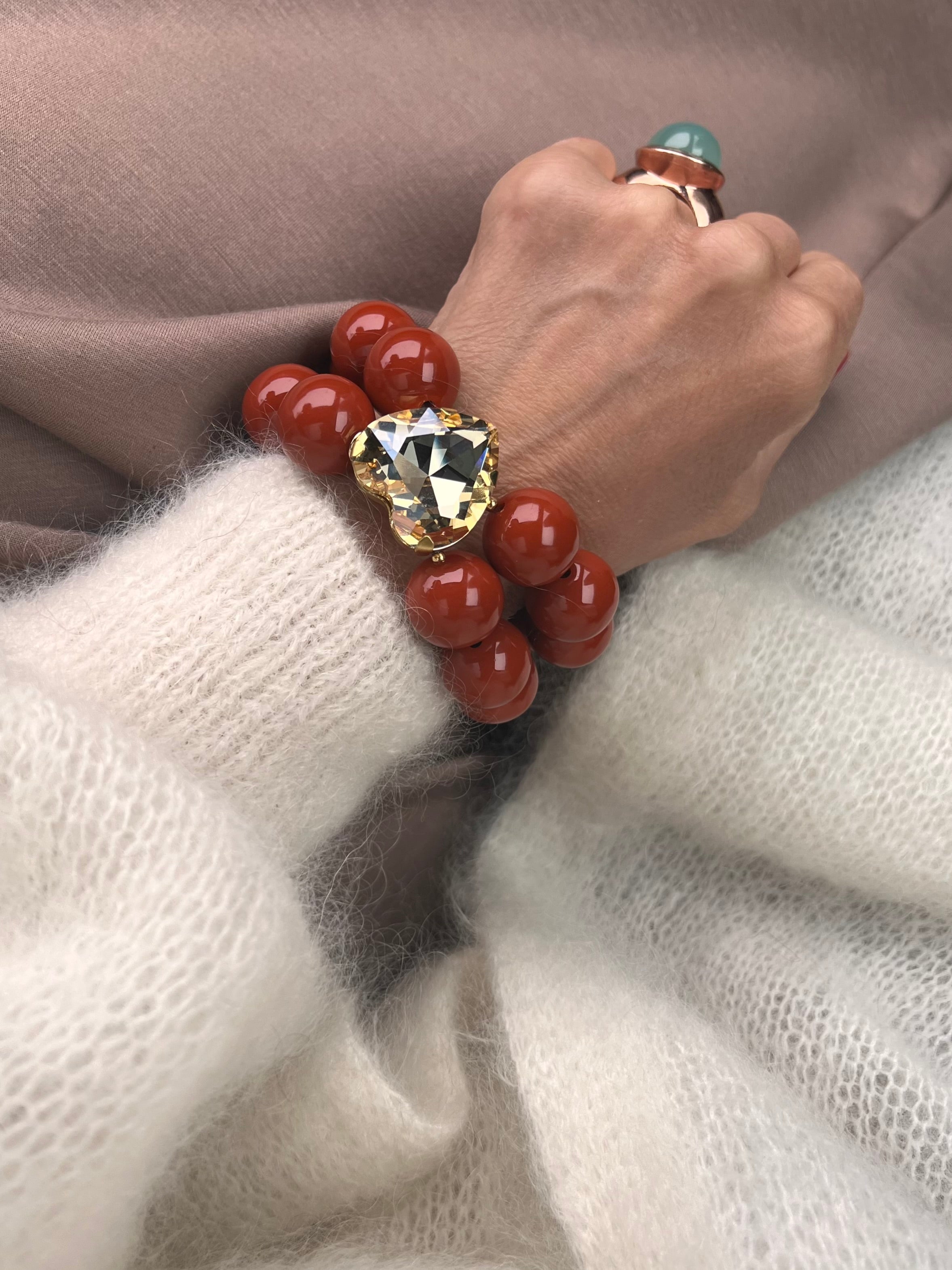 Armband in Karamell mit großem Herzschmuckstein, und großem Ring. Am Handgelenk auf beigem Stoff fotografiert.