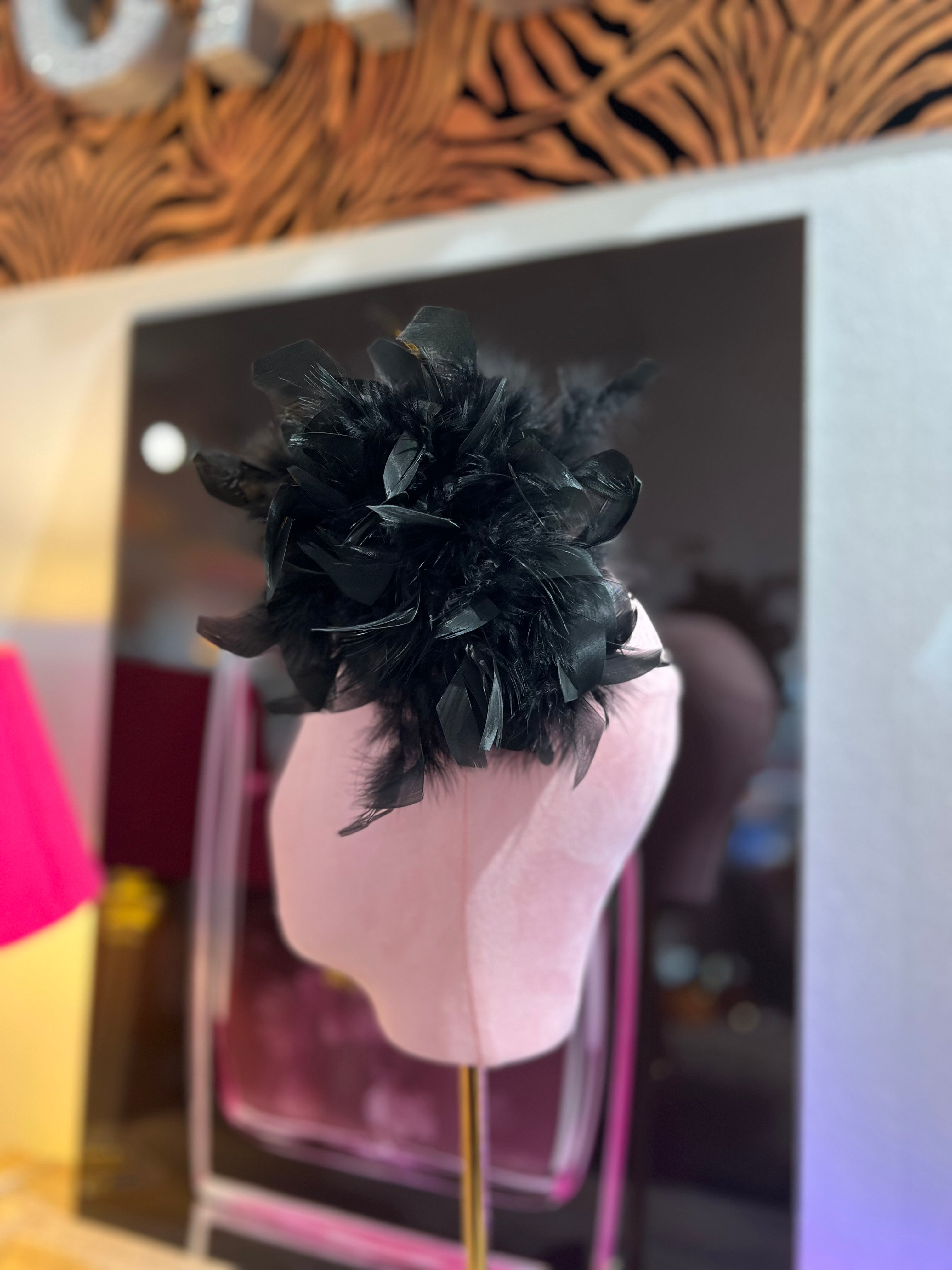 Leuchtende schwarze Federbrosche, kunstvoll drapiert, präsentiert auf einem rosa Samt Kopf vor einer stilvollen Kulisse.