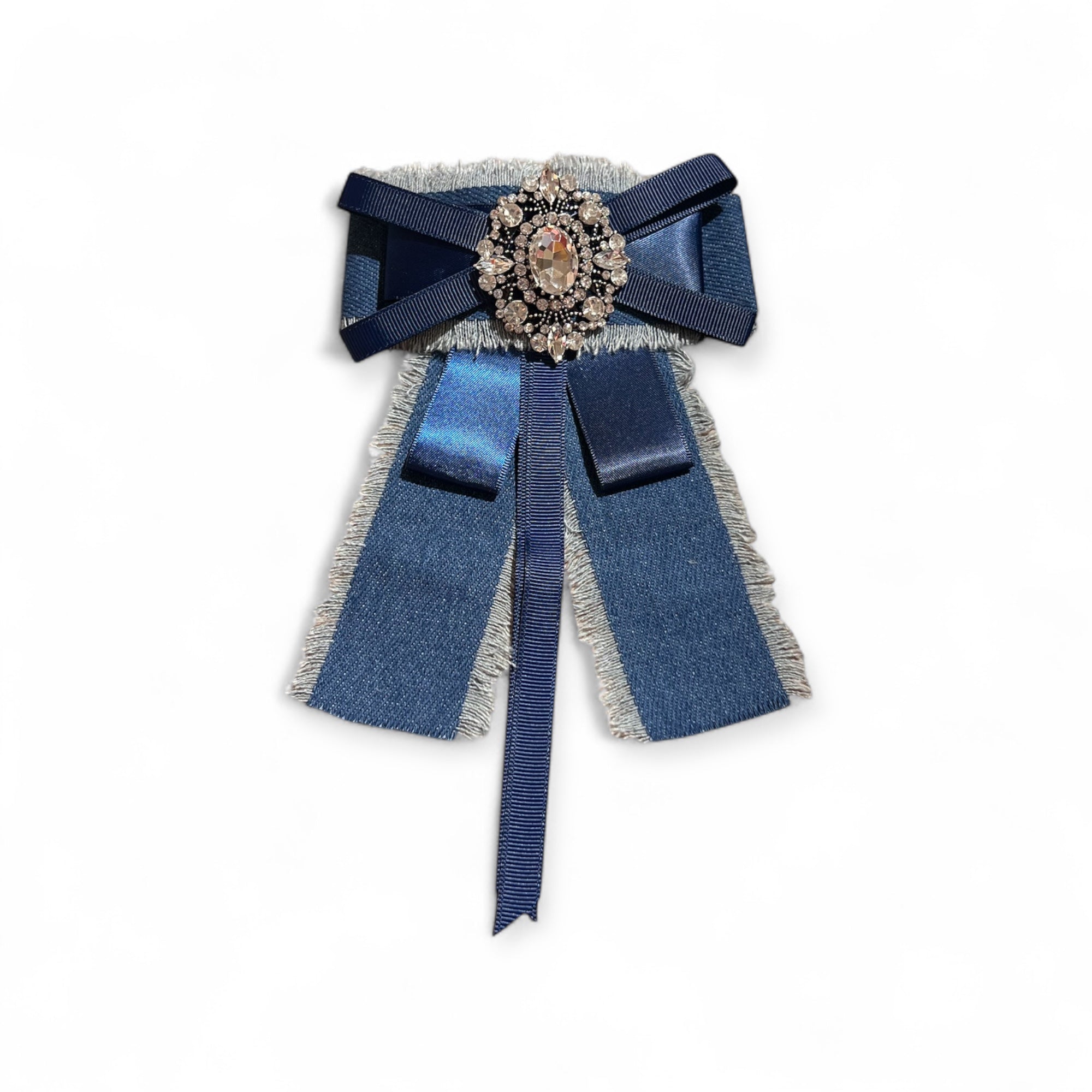 Jeansbrosche mit dunkelblauer Schleife, funkelndem Strasselement in der Mitte uns silbernem Fransenrand. Von vorn aufgenommen auf weißem Hintergrund.