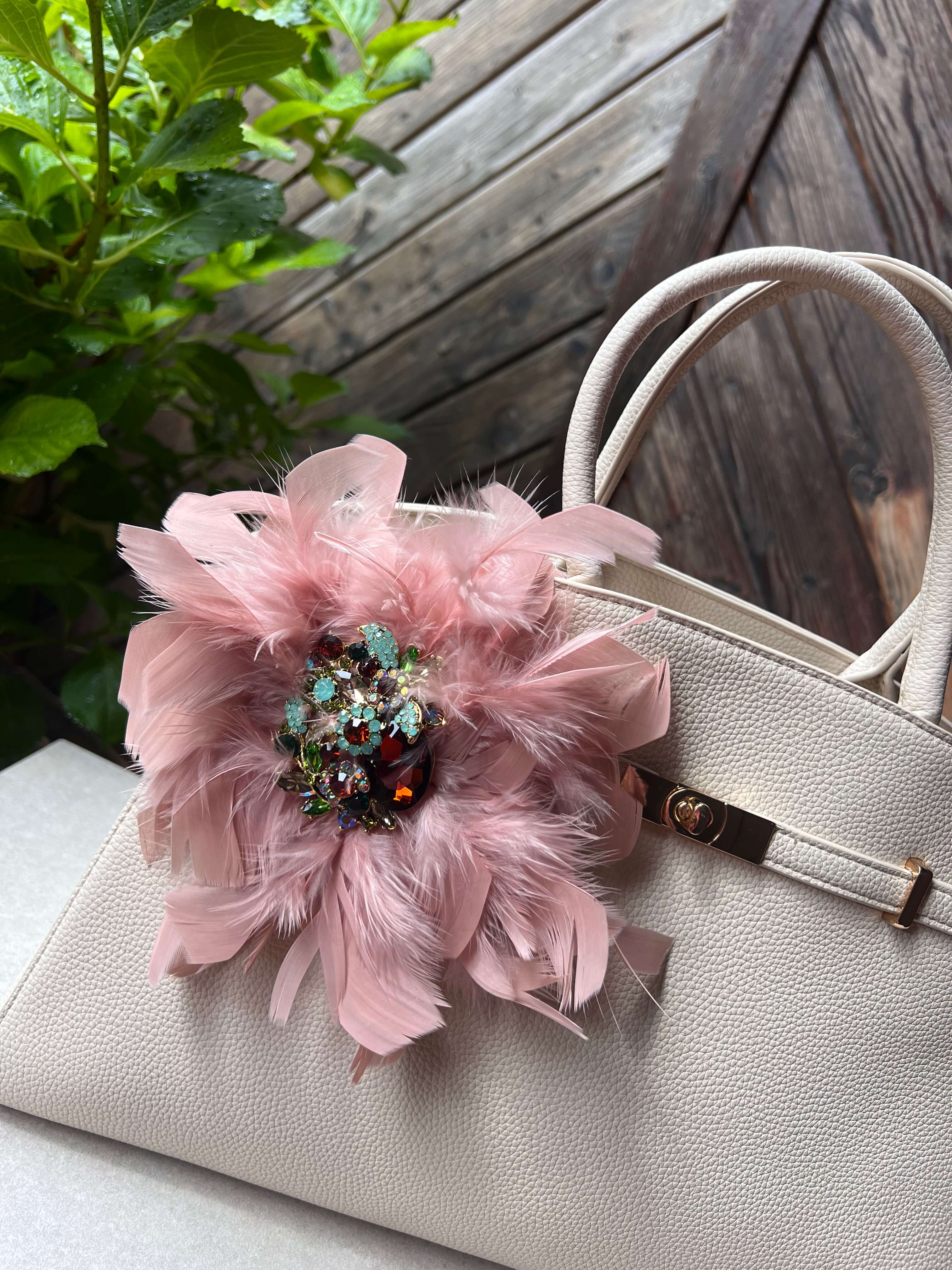 Rose Brosche mit Schmuckelement an einer Beigen Tasche drapiert. Hinter einer Holzwand