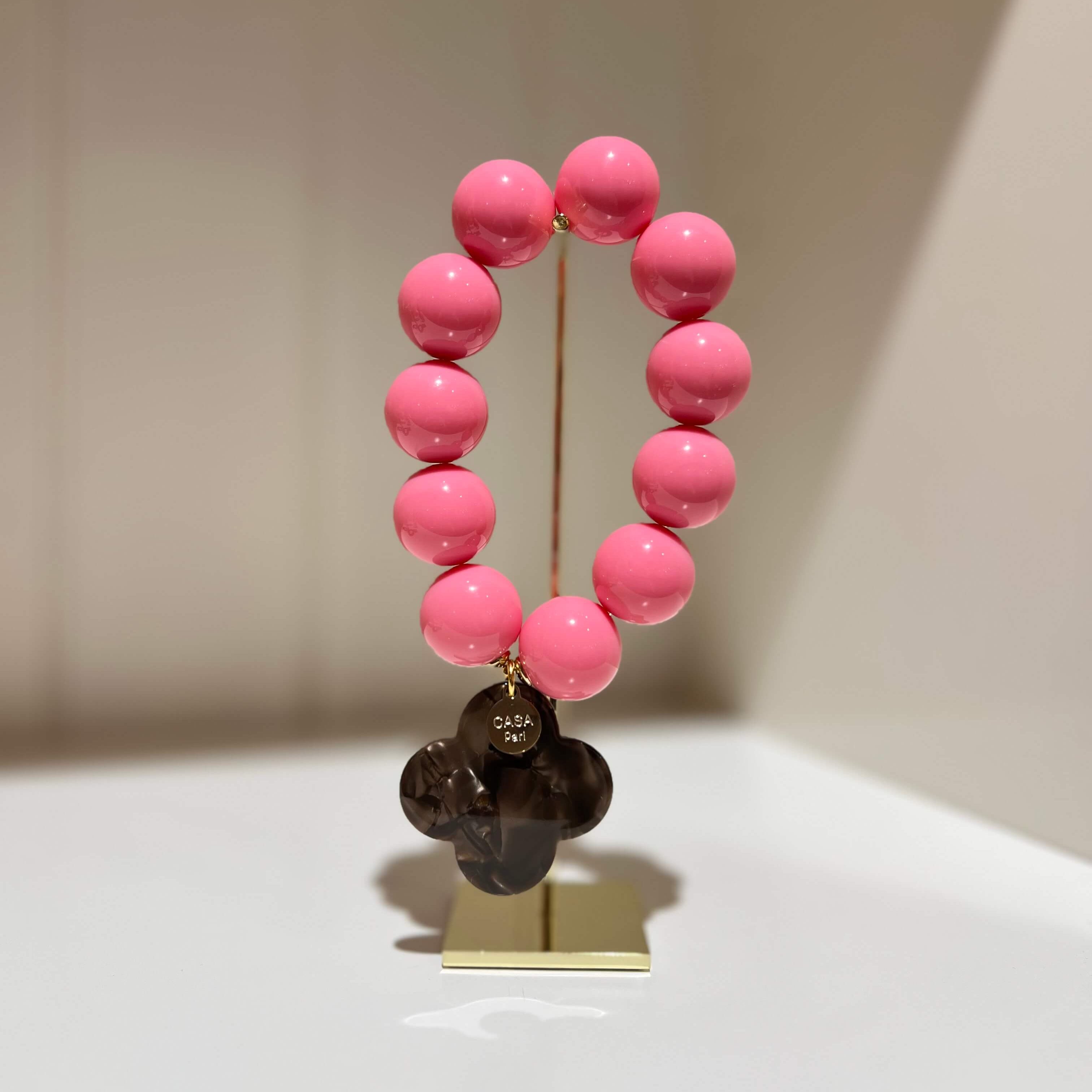 Pinkfarbenes Armband mit runden Perlen und einem dunklen vierblättrigen Anhänger auf einem Schmuckständer.