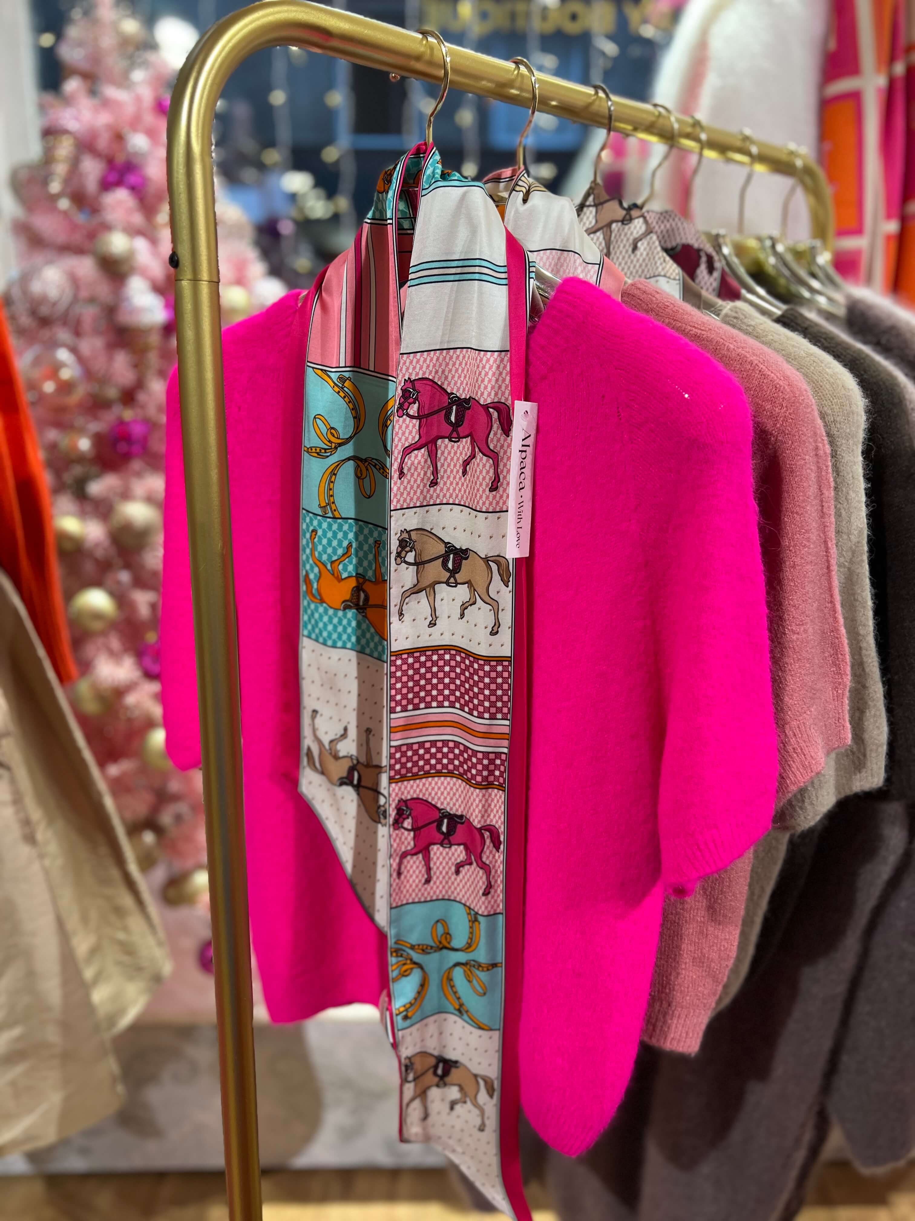 Schmales Seiden-Viskose-Tuch in Pinktönen mit grafischem Muster, an einer goldfarbenen Kleiderstange über einem pinken Strickpullover präsentiert.