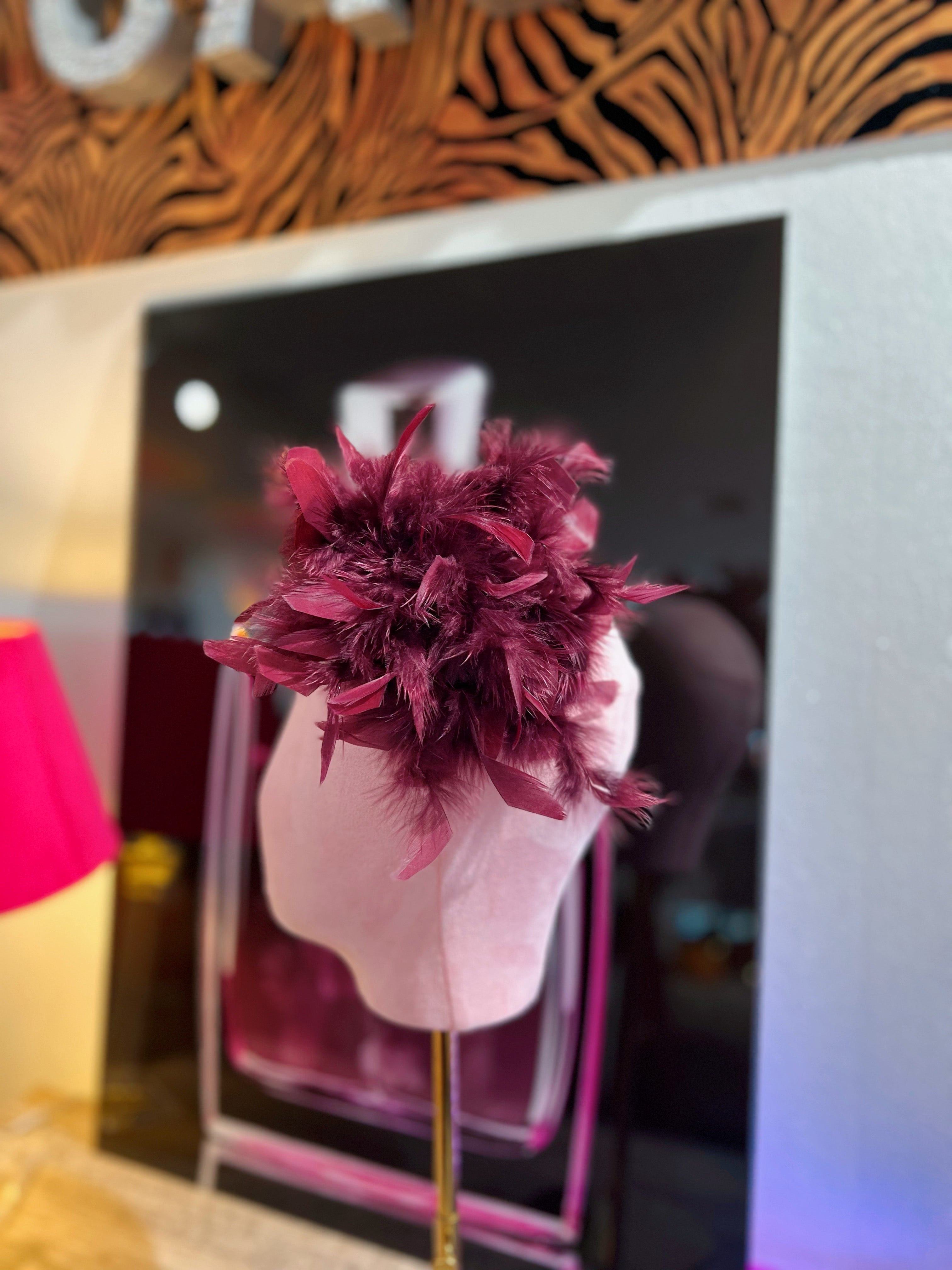 Federbrosche mit großer Blüte aus roten bordeaux farbenen Federn, befestigt auf einer rosa Stoffpuppe vor dekorativen Hintergrund mit Parfumflakon Motiv.