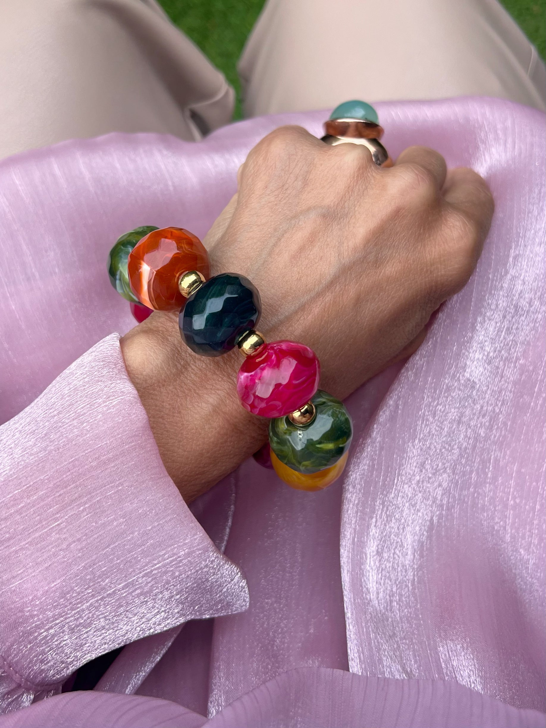 Großes buntes Armband an einem Handgelenk fotografiert auf Rosa Stoff.