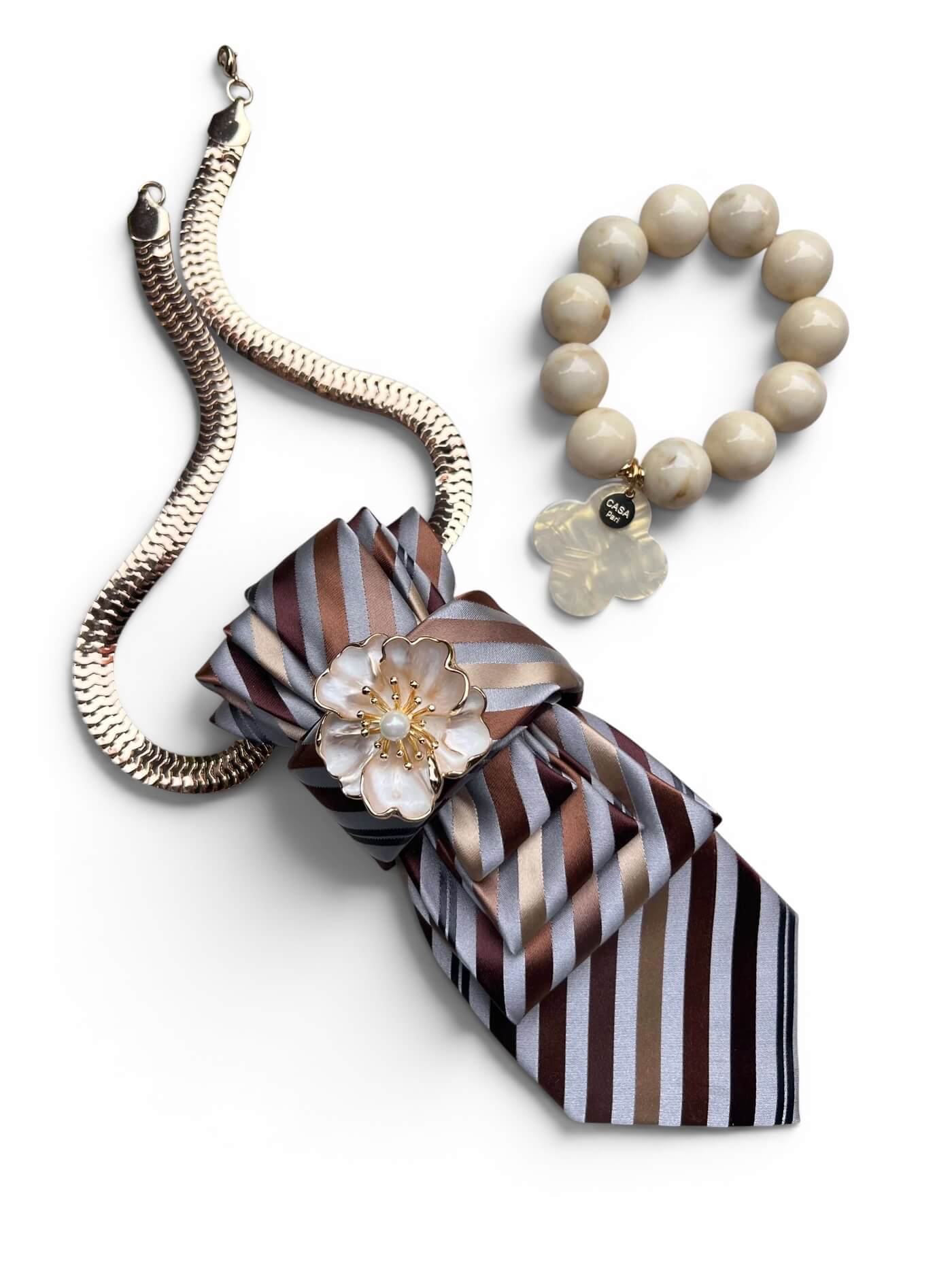 Kombiniertes Set aus gestreifter Krawattenkette mit goldfarbener Kette und Blütenbrosche sowie passendem Armband mit Kleeblatt-Anhänger in Sand-, Creme- und Brauntönen.