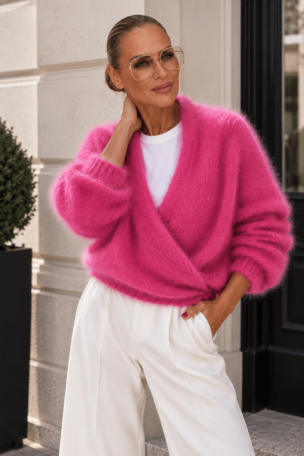 Frau hat eine weiße Hose weiße T-Shirt und einen pinkfarbene Strickjacke an steht auf einer Straße