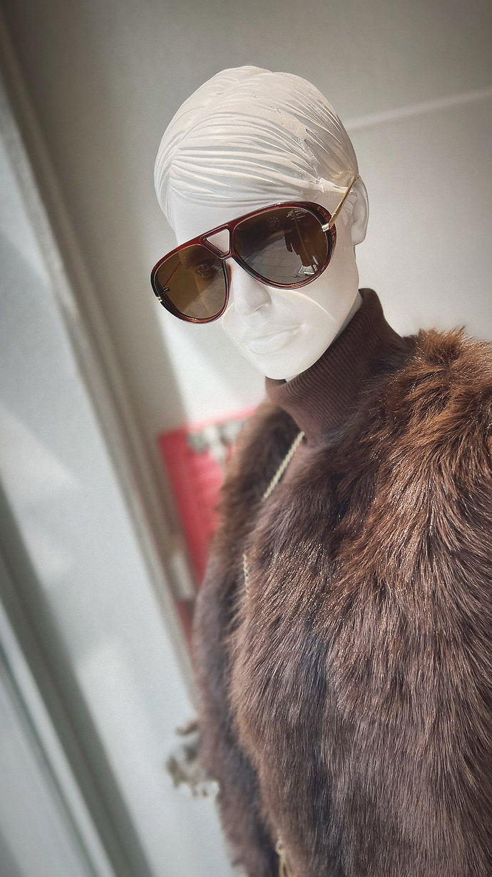 Schaufensterpuppe trägt Sonnenbrille und braunen Rollkragenpulli. Darüber eine braune Fellweste.