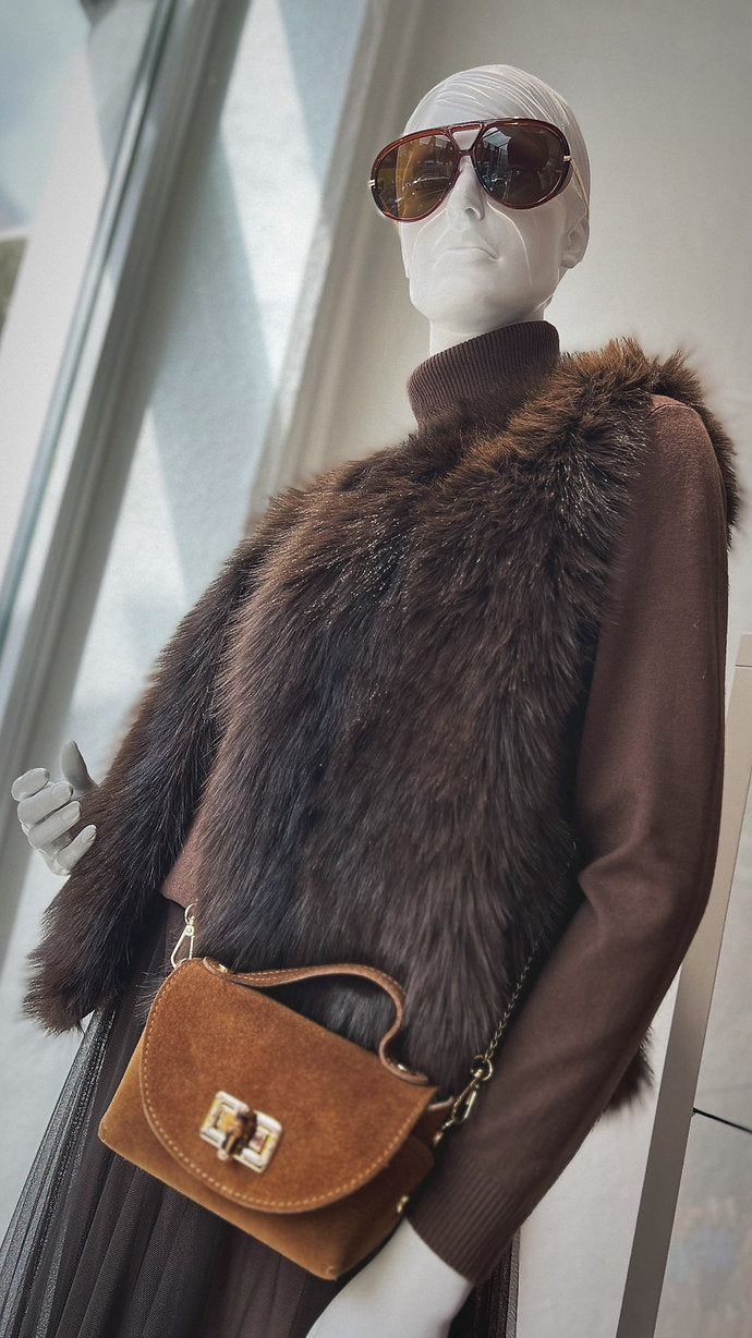 Schaufensterpuppe trägt braune Fellweste mit Rollkragenpulli. Braune Schultertasche mit goldenen Details.