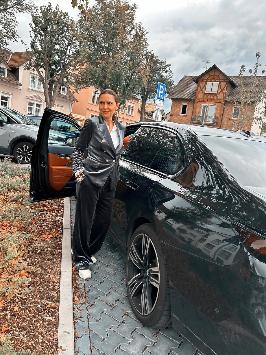 Frau trägt Samt Anzug mit goldenen Knöpfen. Am Auto stehend. Fotografiert an Häuser.