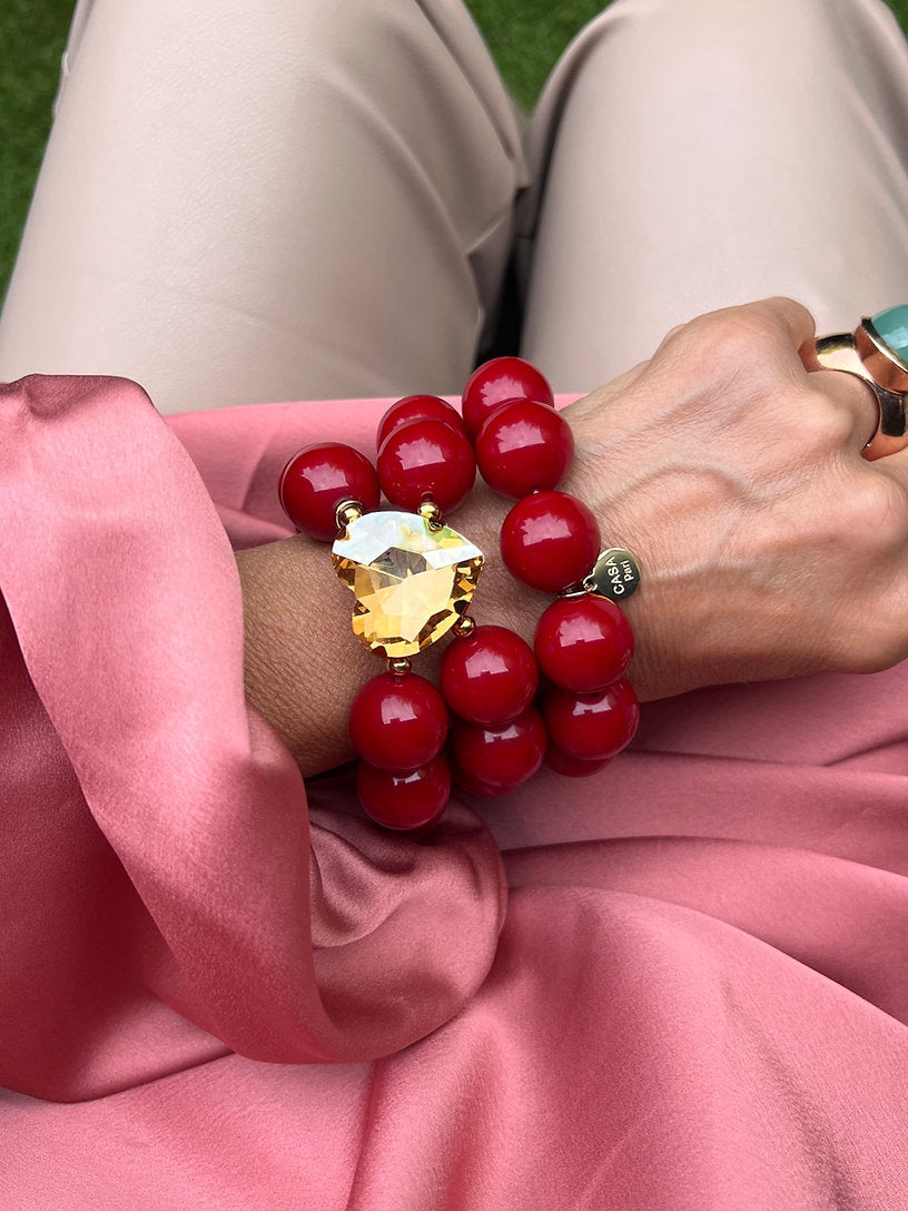 Handgelenk mit auffälligem Armband aus großen roten Perlen und einem großen topasfarbenen Kristall, kombiniert mit einem Statement Ring mit türkisfarbenen Stein. Dazu ein Armband in der gleichen Farbe.