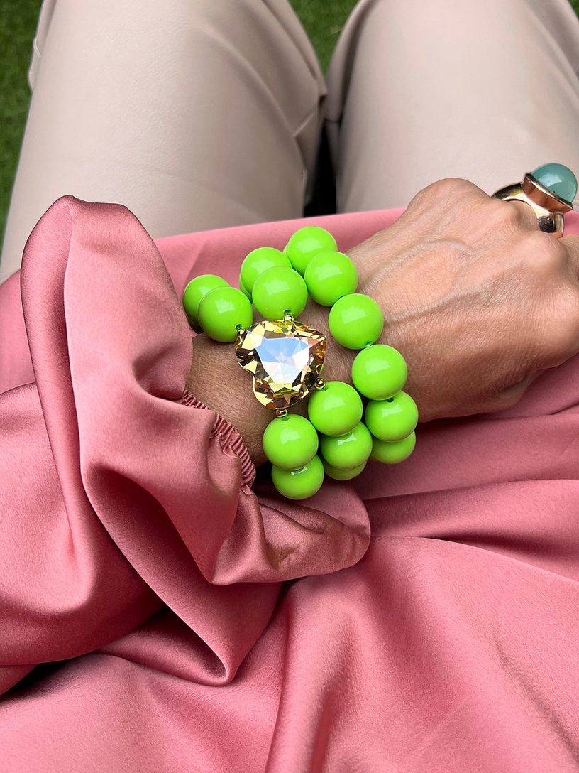 Grüne Armbänder aus Perlen mit Kristall Herz in der Mitte. An Hand auf rosa Stoff.