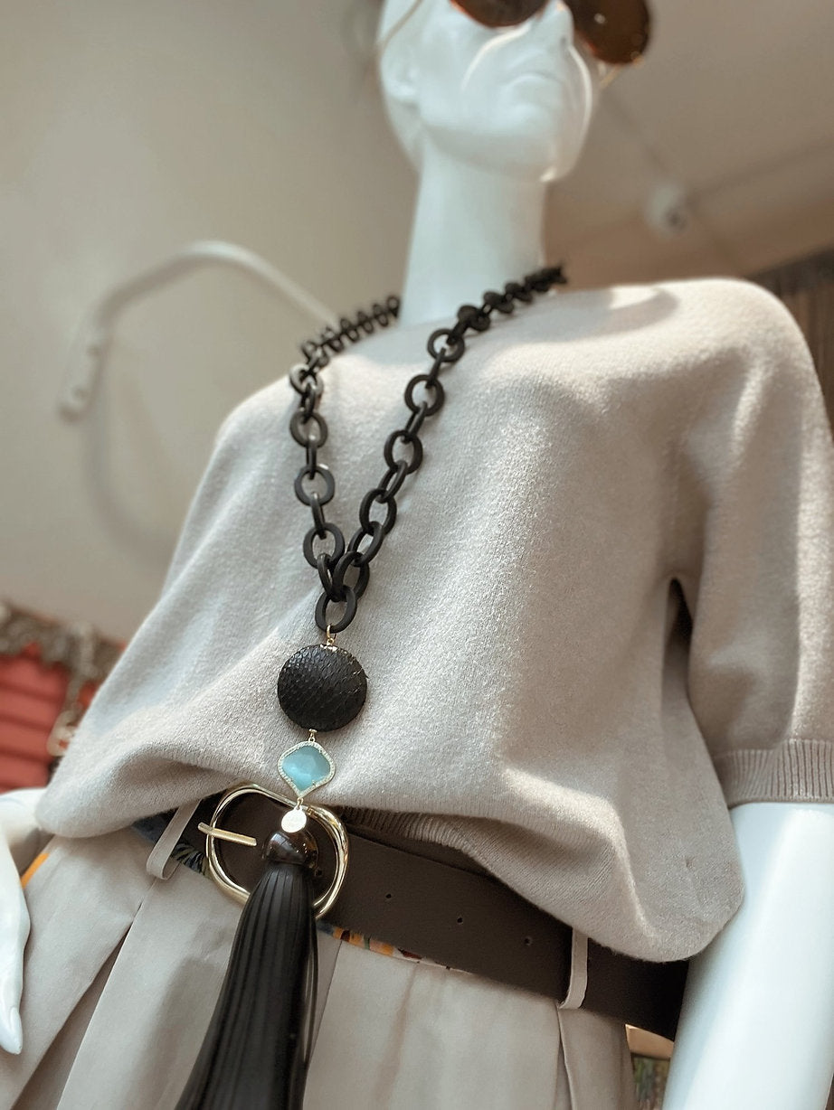 Schaufensterpuppe mit langer Kette und Ledertroddel. Sonnenbrille und brauner Gürtel. Beigefarbener Pulli.