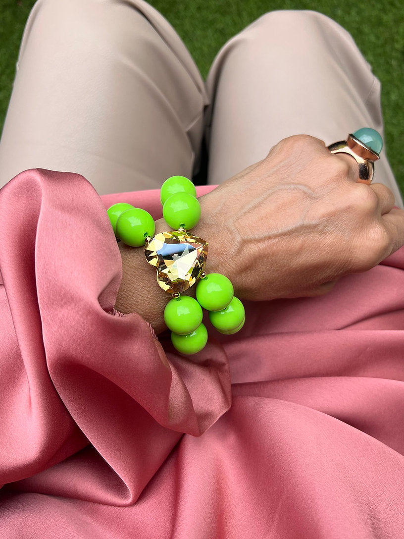 Grünes doppelreihiges  Perlenarmband mit goldenem Herz. Dekoriert am Handgelenk auf Rosa Stoff.