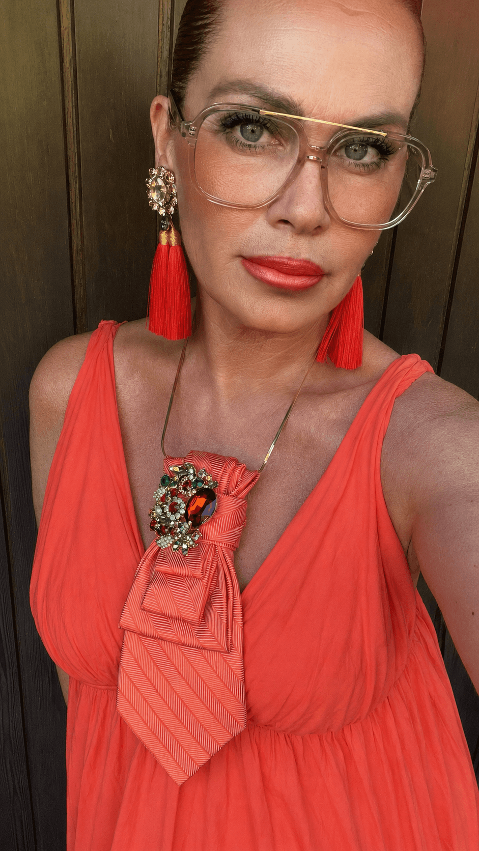 Frau mit korallfarbenem Sommerkleid, roten Quastenohrringen und korallfarbener Casapari-Krawatte mit Schmuckbrosche.