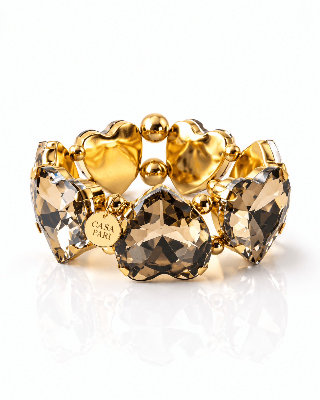 Crystal Heart The Grand One Armband von CASA PARI mit großen facettierten Kristallherzen in Champagner, goldfarbenen Edelstahlperlen und rundem Logo-Anhänger.