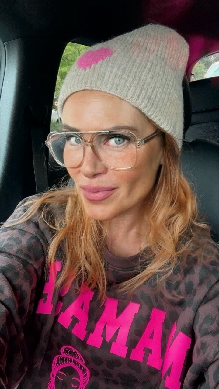 Frau trägt eine beige Strick-Beanie mit pinkfarbenem Herz, transparente Brille und ein Leo-Sweatshirt mit pinkem Statement-Print.