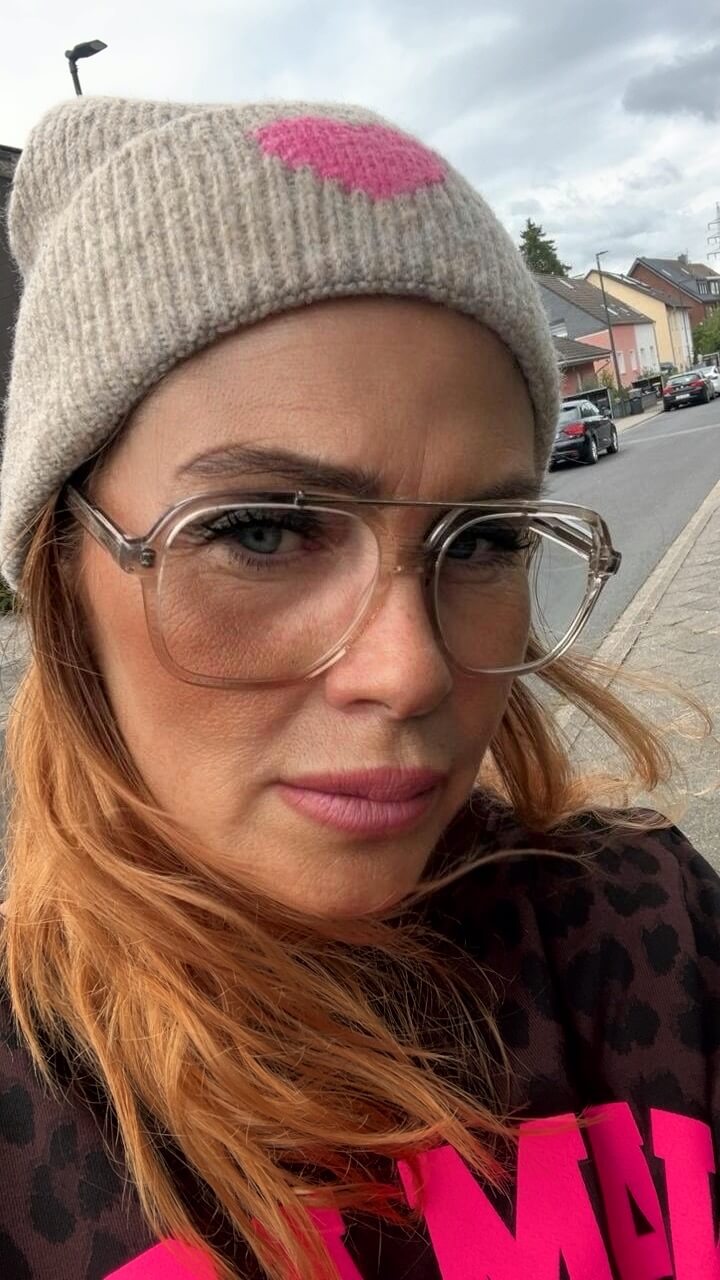 Nahaufnahme einer Frau mit transparenter Brille und grauer CASAPARI Strick-Beanie mit pinkem Herz.