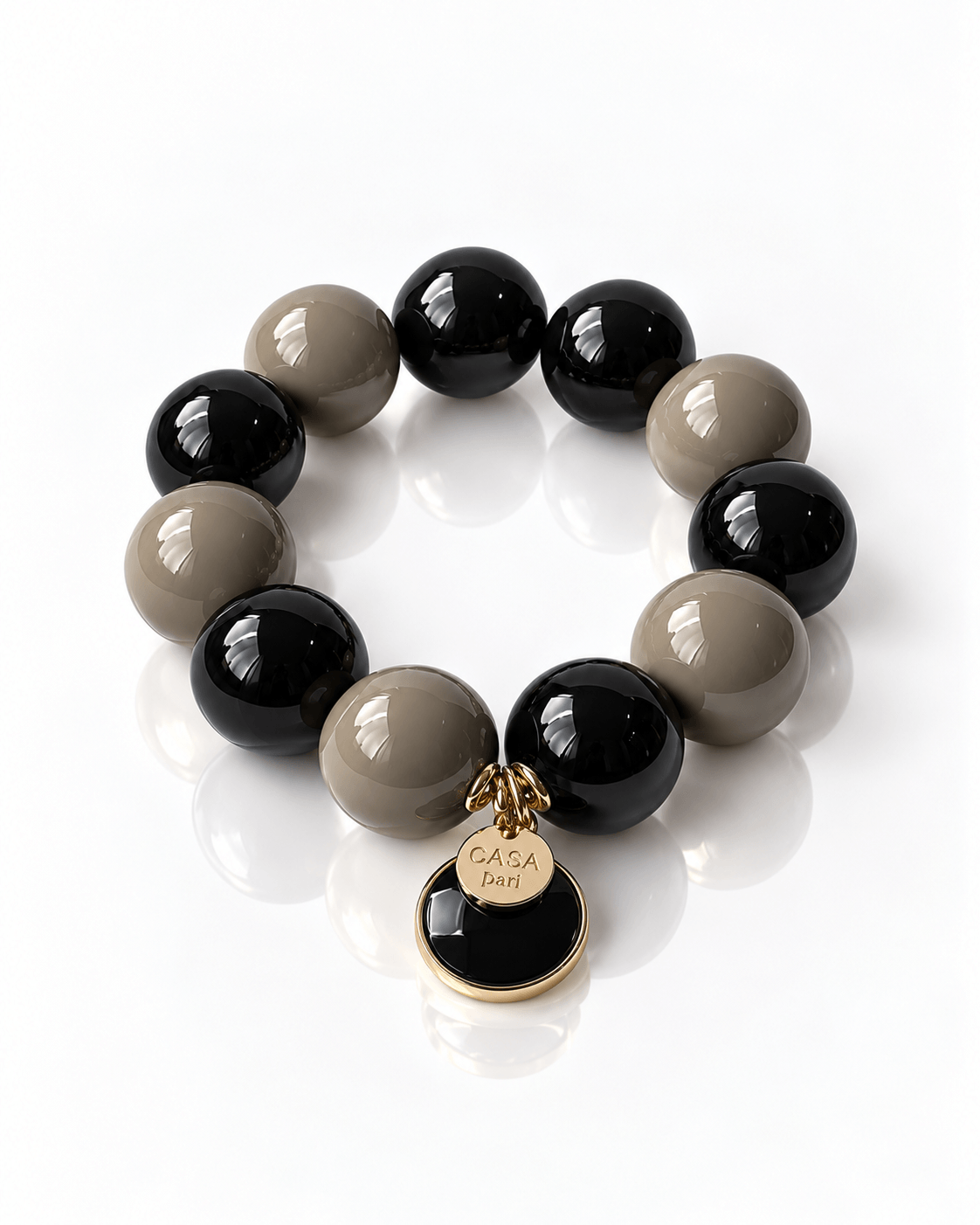 Armband aus großen Resin-Perlen in Cashmere Mocca und Schwarz mit rundem Onyx-Anhänger und goldfarbenem Casapari Charm.