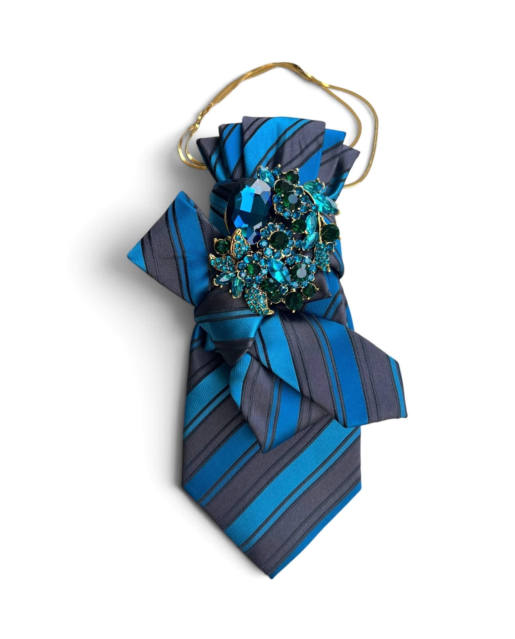 Blau-grau gestreifte Statement-Krawatte aus Vintage-Seide mit dekorativer Schleife, funkelnder Brosche in Blau- und Grüntönen sowie eleganter Goldkette.