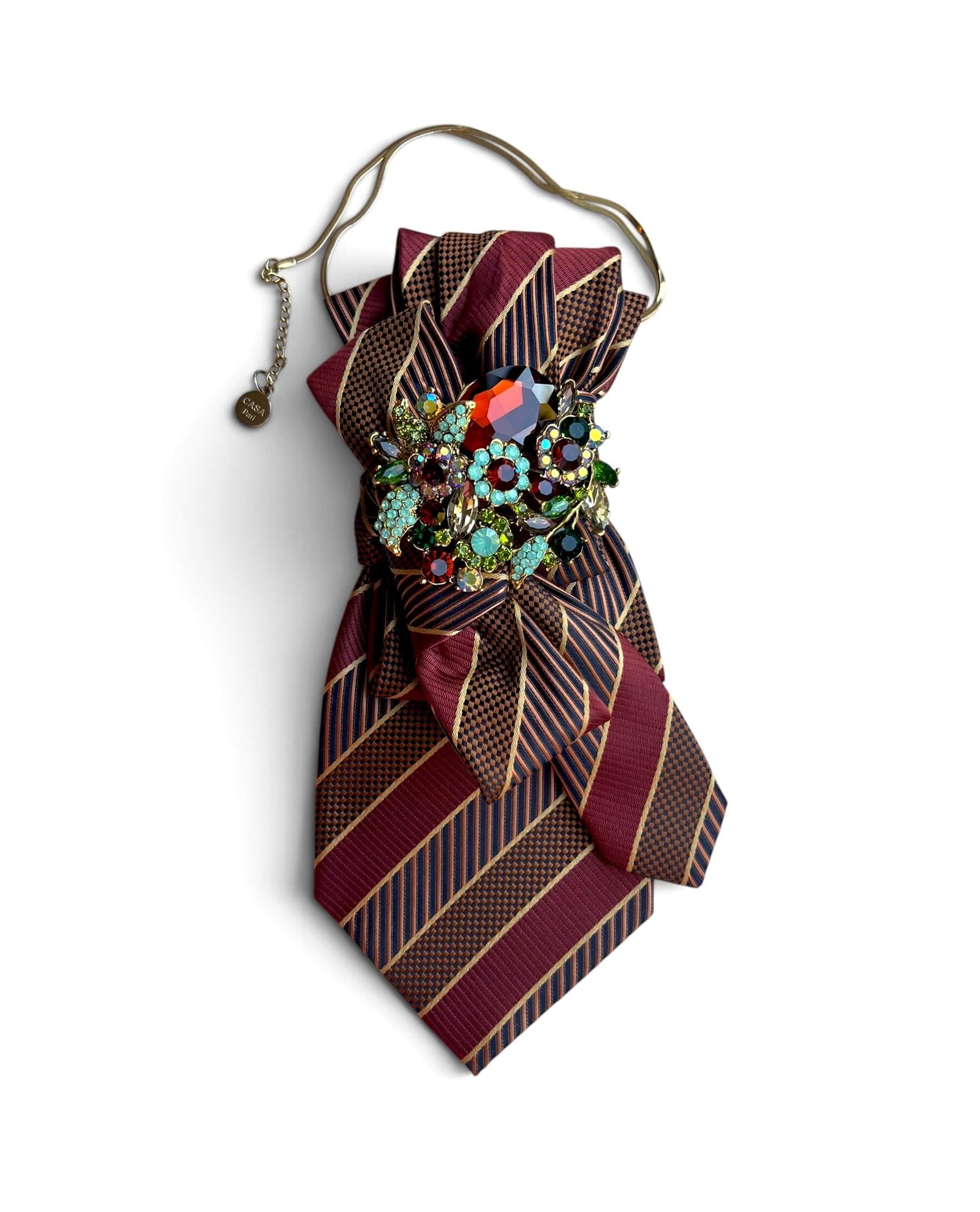Statement-Krawatte aus Vintage-Seide in Bordeaux, Navy und Gold mit Schleife sowie opulenter Schmuckbrosche an goldfarbener Kette.