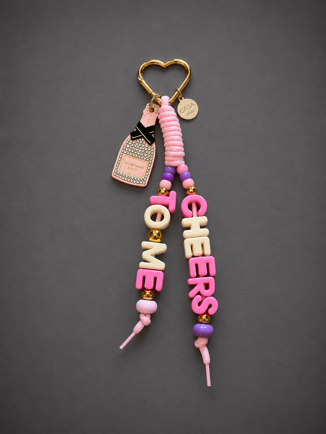 Roséfarbener CASA PARI Champagne Diet Bag Charm mit pink-cremefarbenen Letter-Straps, Strass-Charm, goldfarbenen Details und Herz-Karabiner