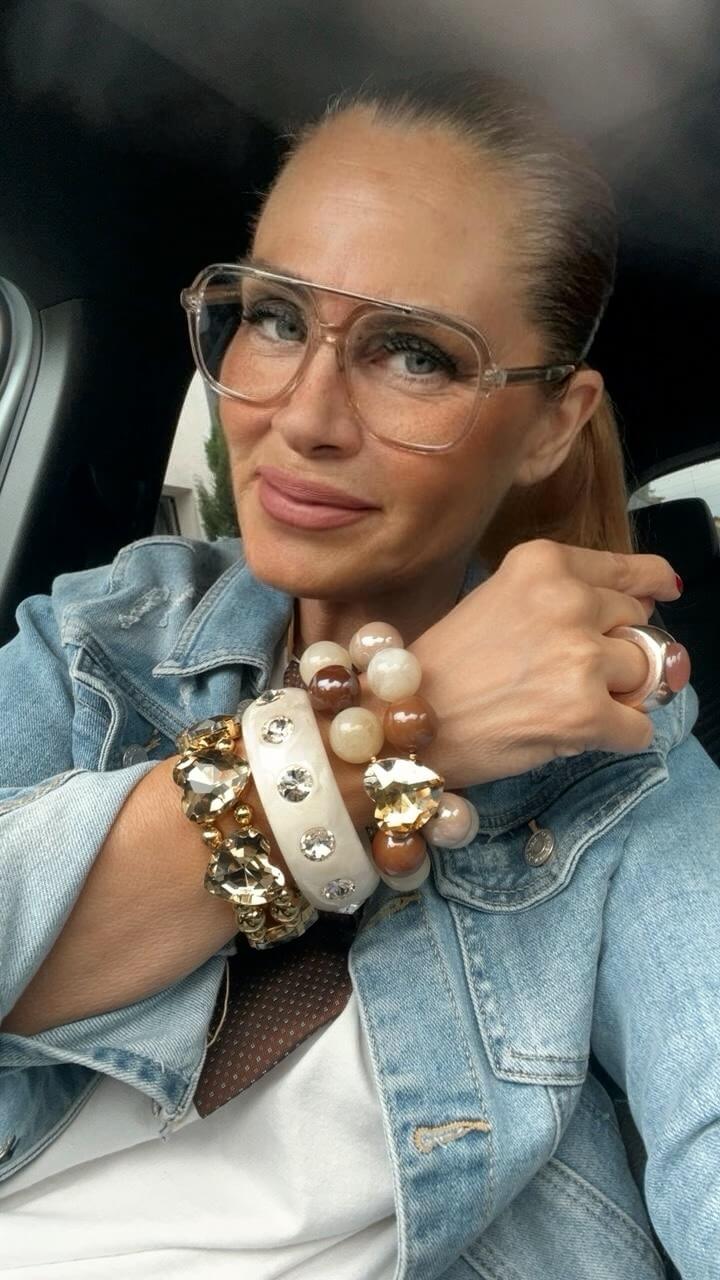 Frau mit drei übereinander getragenen Statement-Armbändern in Creme, Champagner und warmen Brauntönen mit großen funkelnden Kristallherzen.