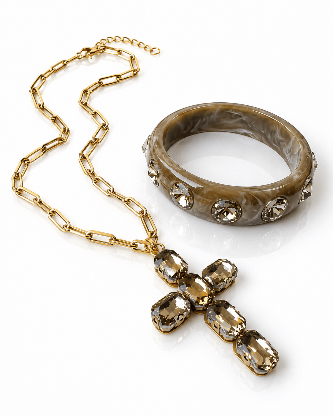 Goldfarbene Edelstahlkette mit großem Kristallkreuz und marmorierter Resin-Armreif mit champagnerfarbenen Kristallsteinen.