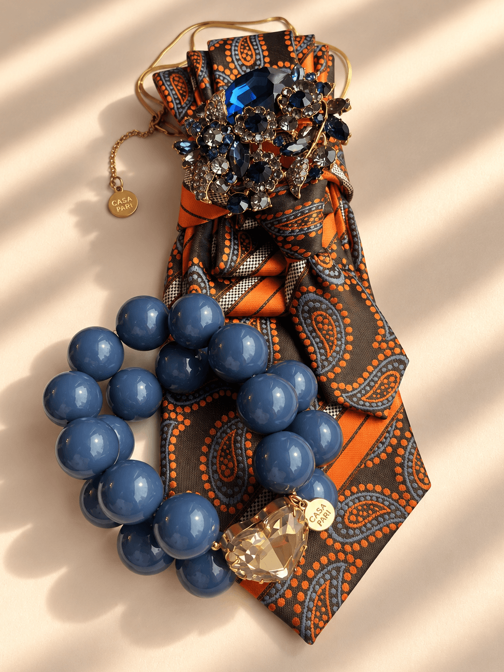Casa Pari Crystal Heart Armband Denim Smoke kombiniert mit orange-brauner Paisley-Krawatte und Schmuckdetail