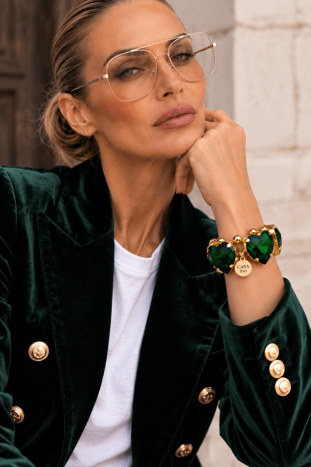Frau trägt ein großes Crystal Heart Armband mit grünen facettierten Herzen und goldfarbenen Details zu einem smaragdgrünen Samtblazer.